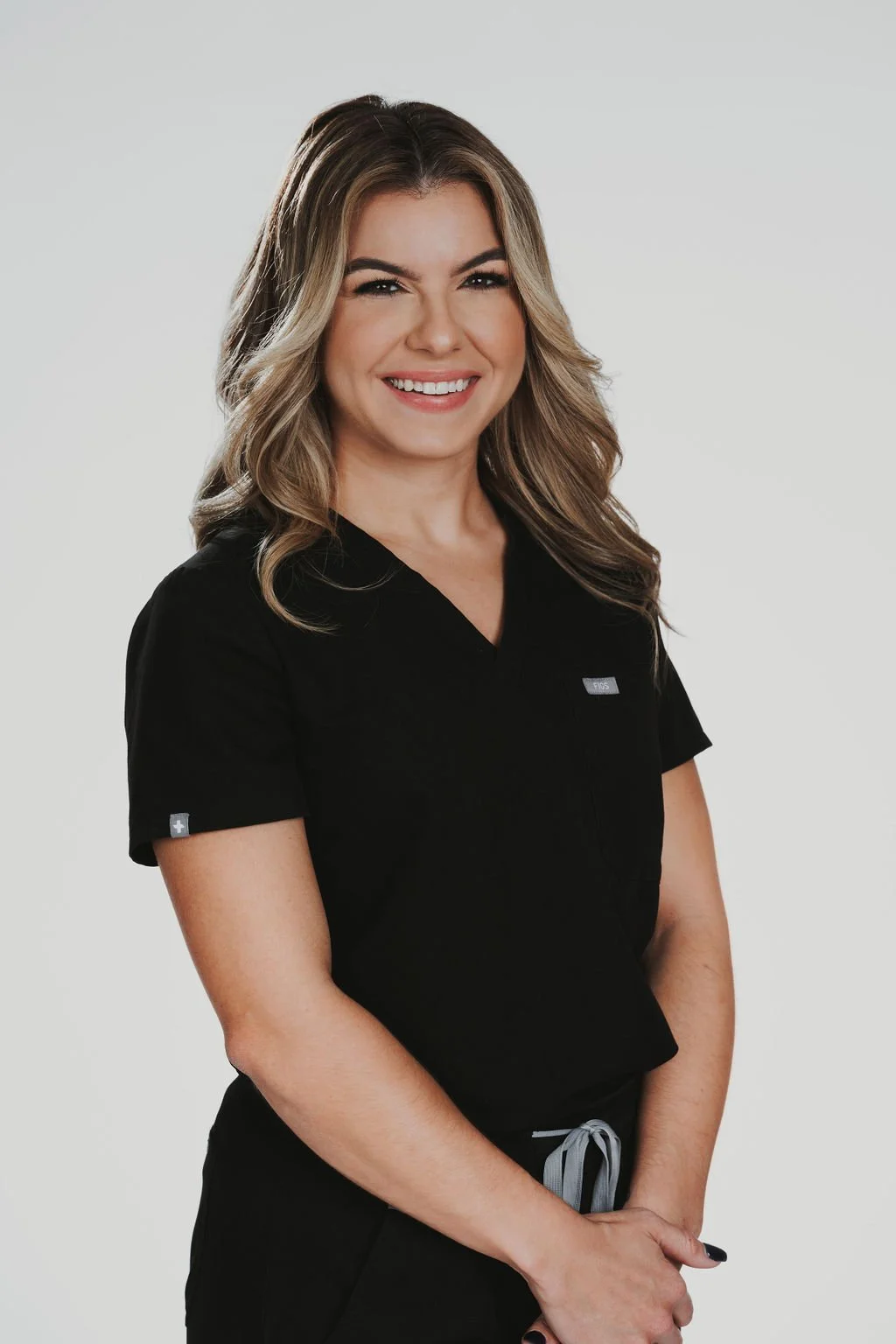 Person smiling in black medical scrubs against a plain background.