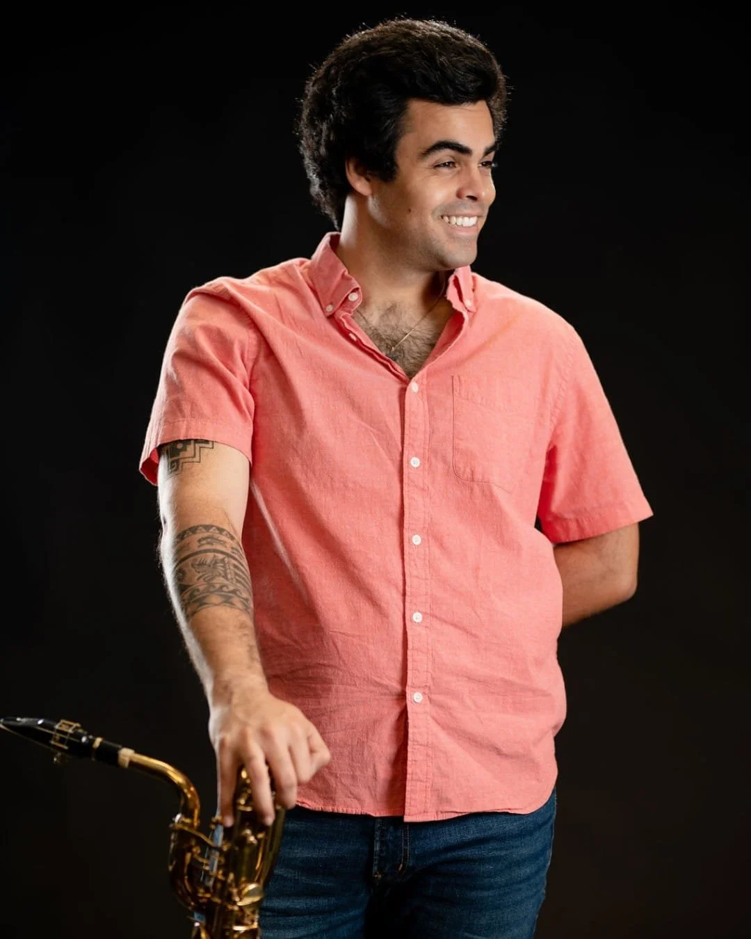 Man in a pink shirt with a tattoo on his arm holding a saxophone.