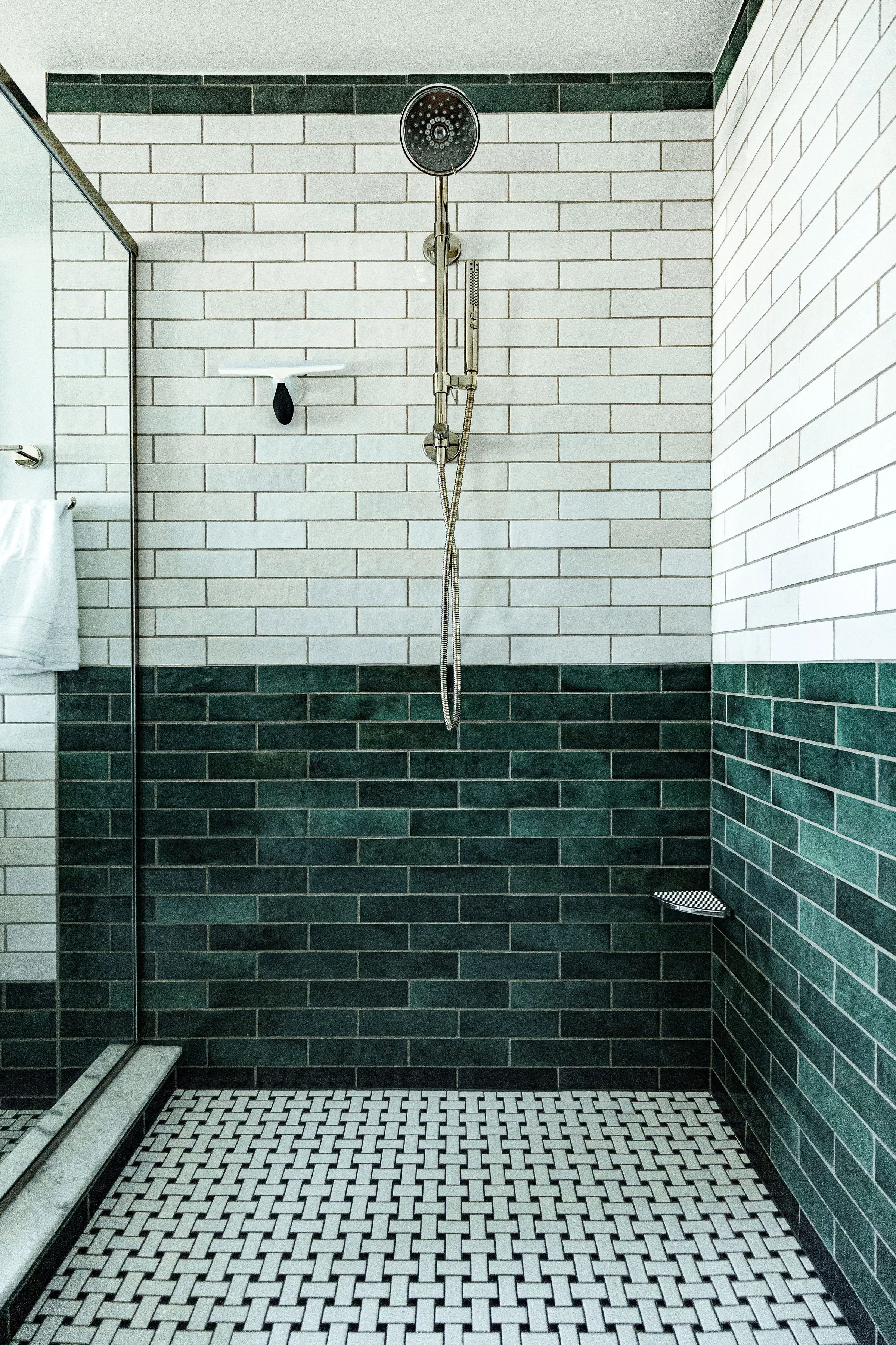 Empty shower with black and white tiled floor, white and green tiled walls, and a chrome showerhead.
