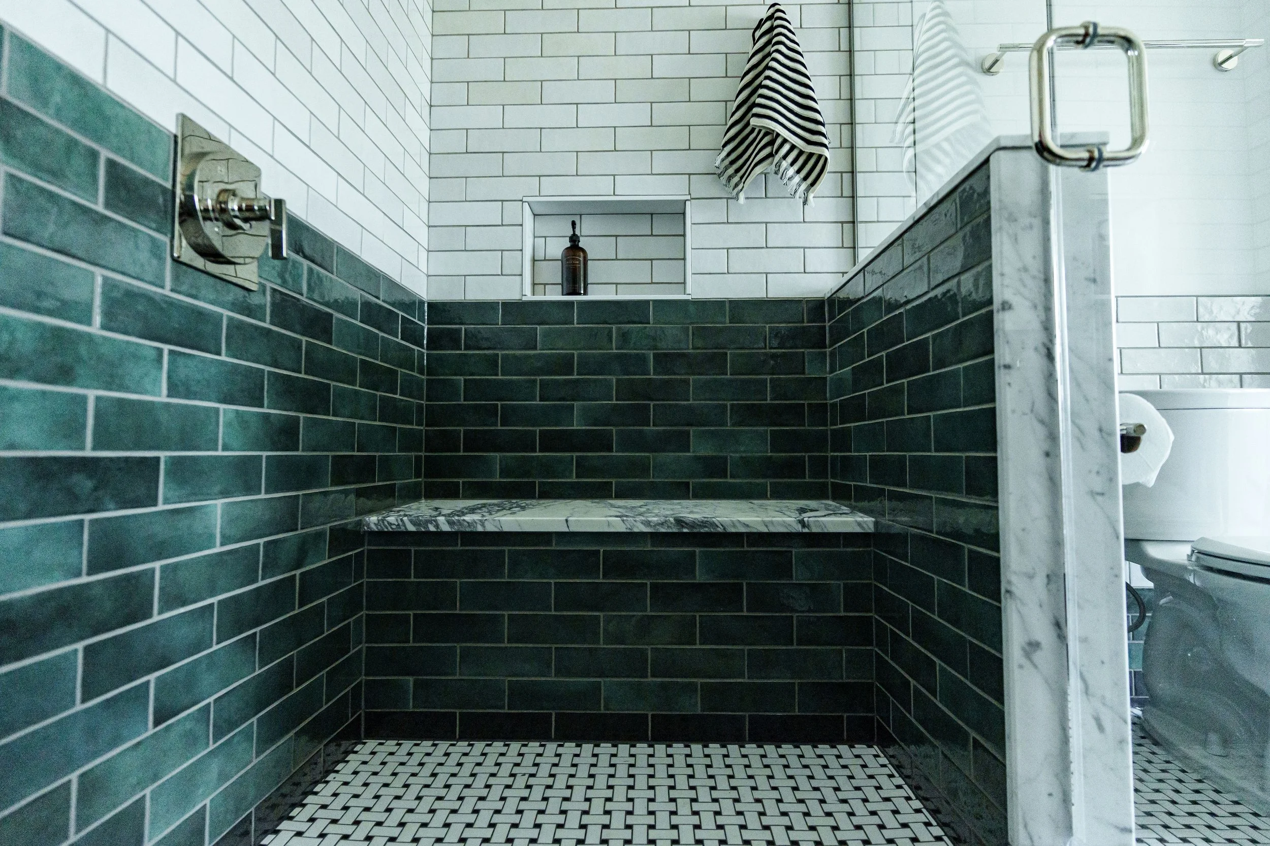 Modern bathroom shower area with green subway tiles, white subway tiles, a marble ledge, and a toilet visible in the corner.