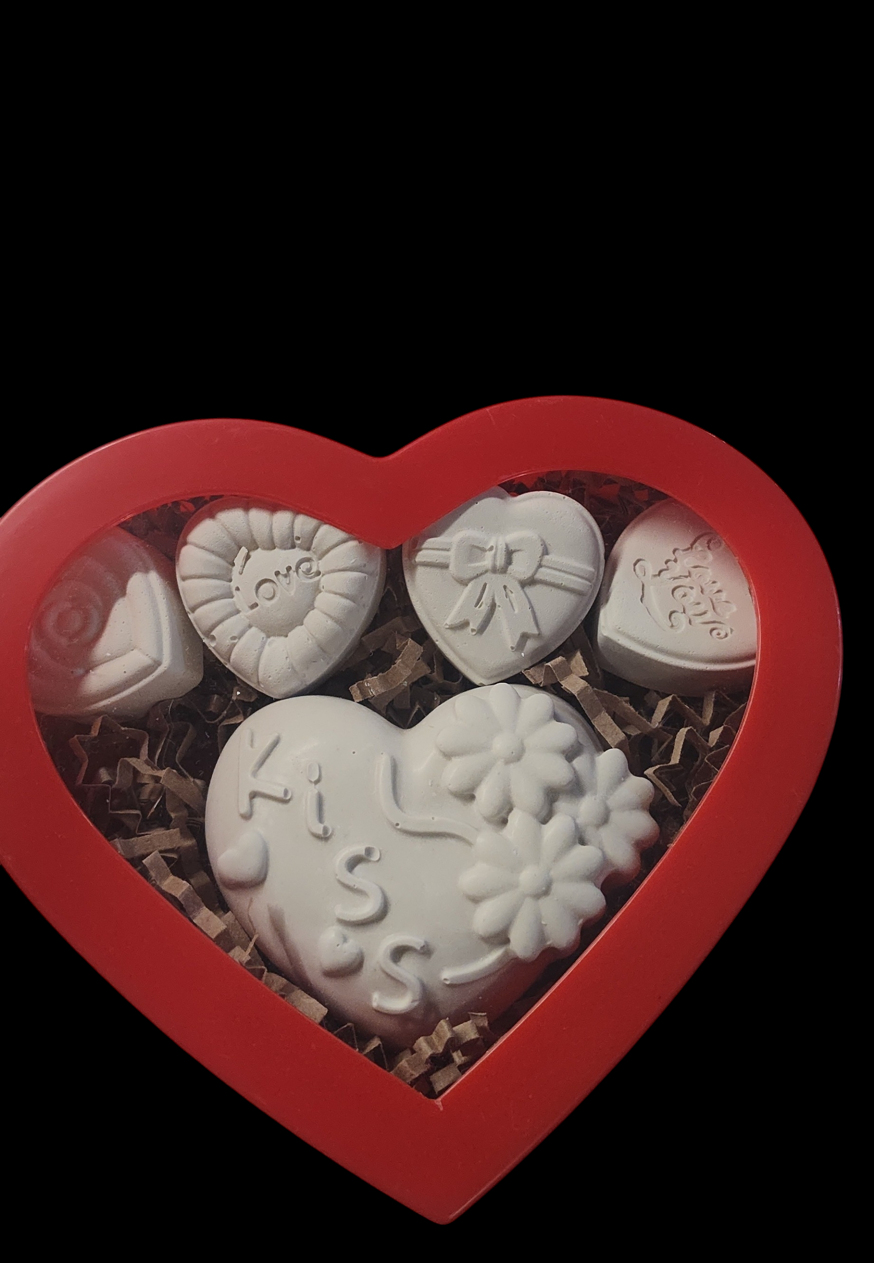 A plastic red heart chapped box filled with brown shredded paper with four small heart magnets with one large heart magnet.