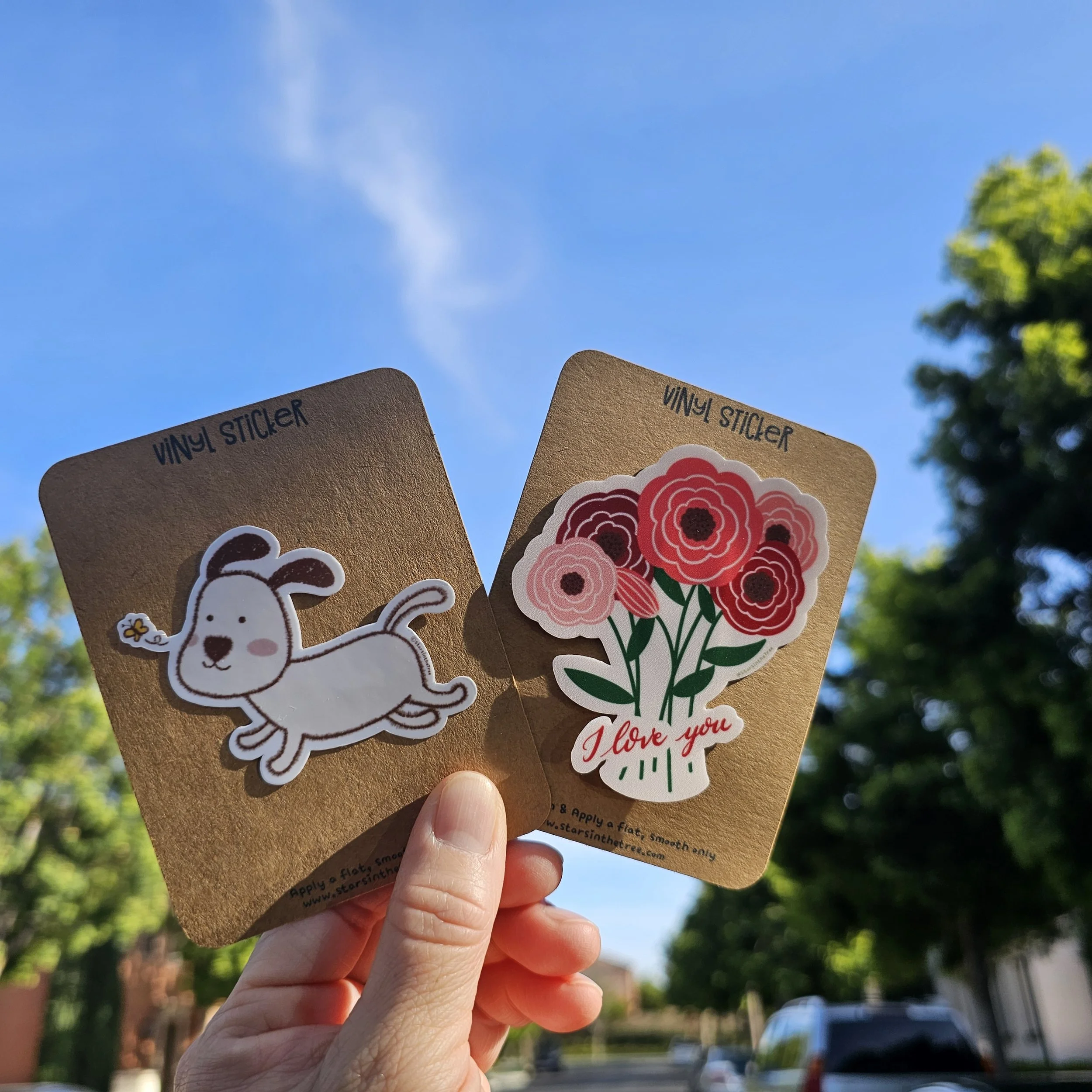 Two vinyl stickers: one features a cute white dog with brown patches and a small yellow flower on its ear, the other has a bouquet of pink and red flowers with a caption 'I love you'.