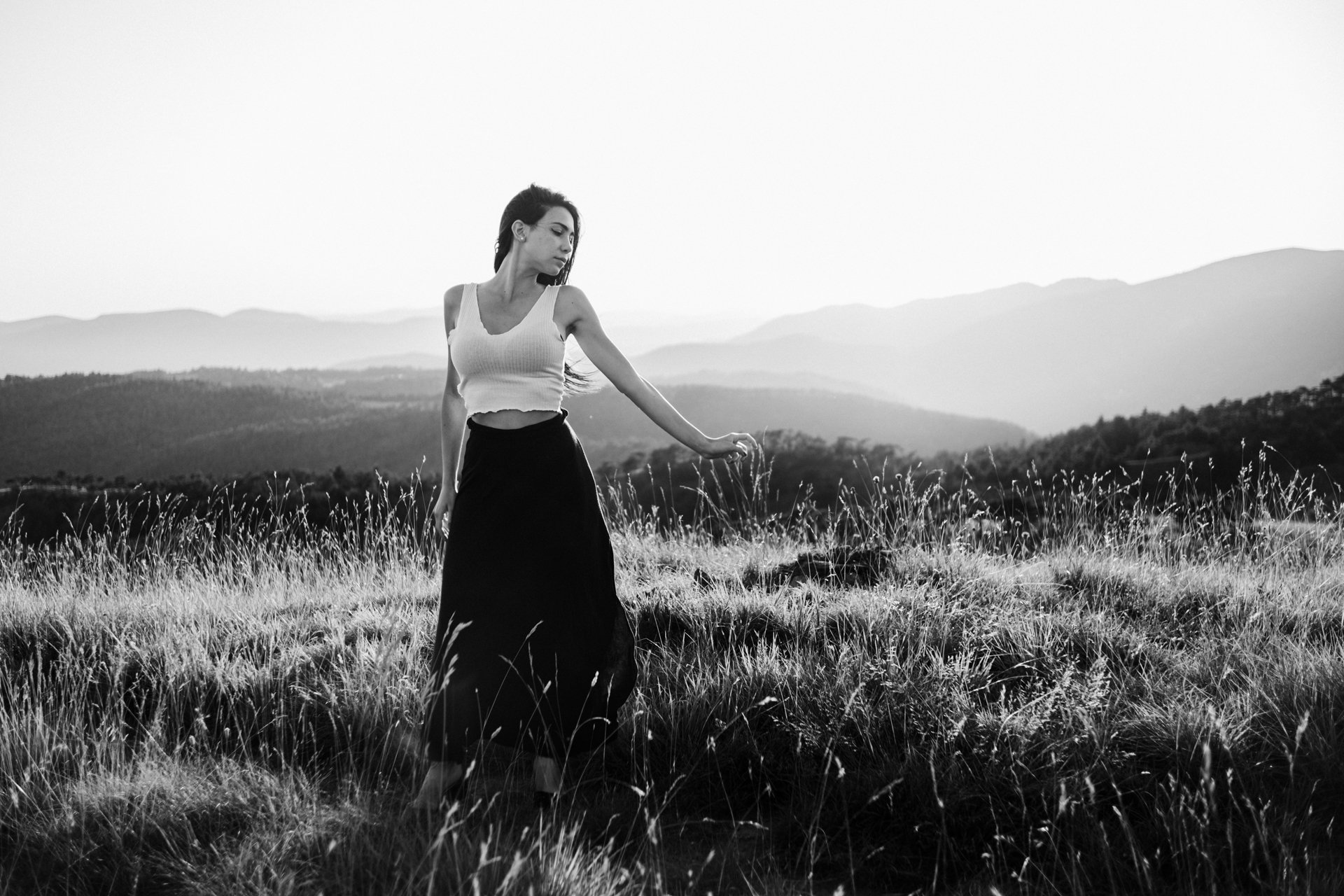 Donna in abito nero e top bianco che cammina in un campo di erba con sfondo di montagne in bianco e nero.