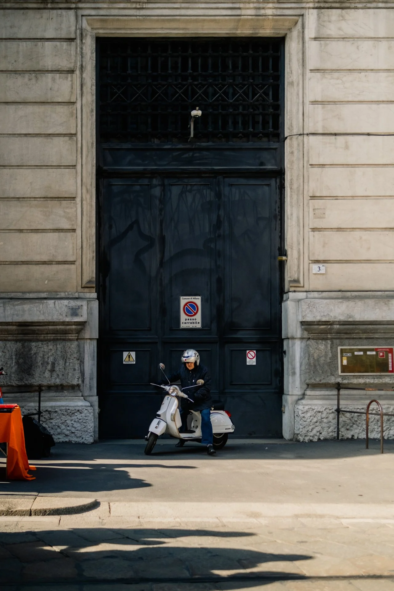 Persona su scooter nero davanti a un grande cancello nero di una costruzione storica in pietra