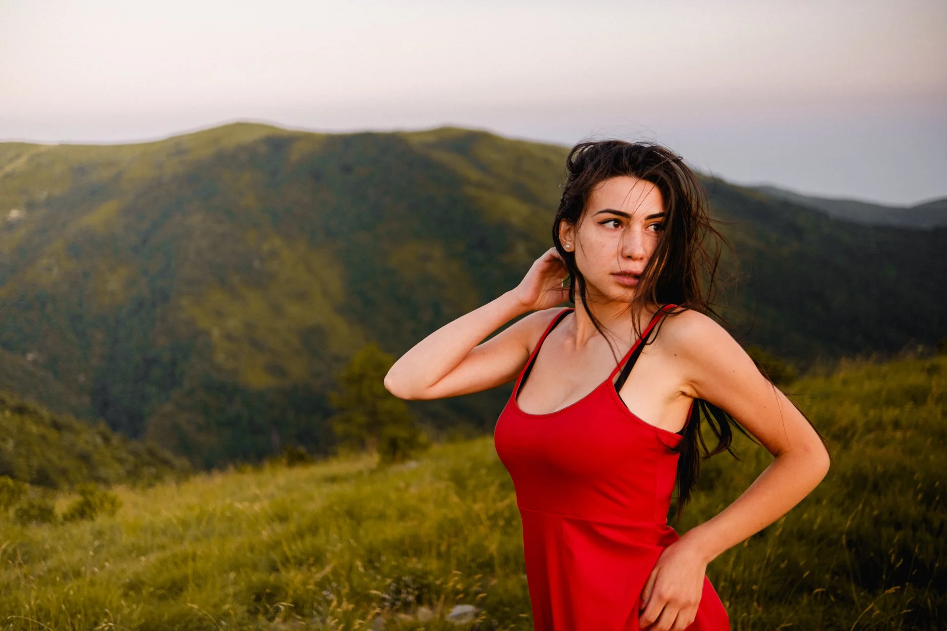 Una donna con vestito rosso in un paesaggio montano durante il tramonto.