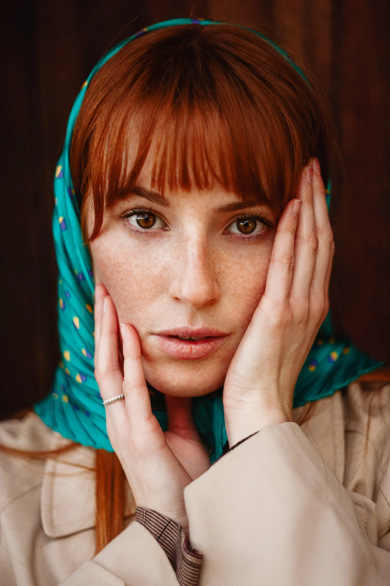 Ragazza con capelli castano-rossi, indossa un foulard azzurro con disegni colorati, con le mani sulla faccia, sfondo scuro.