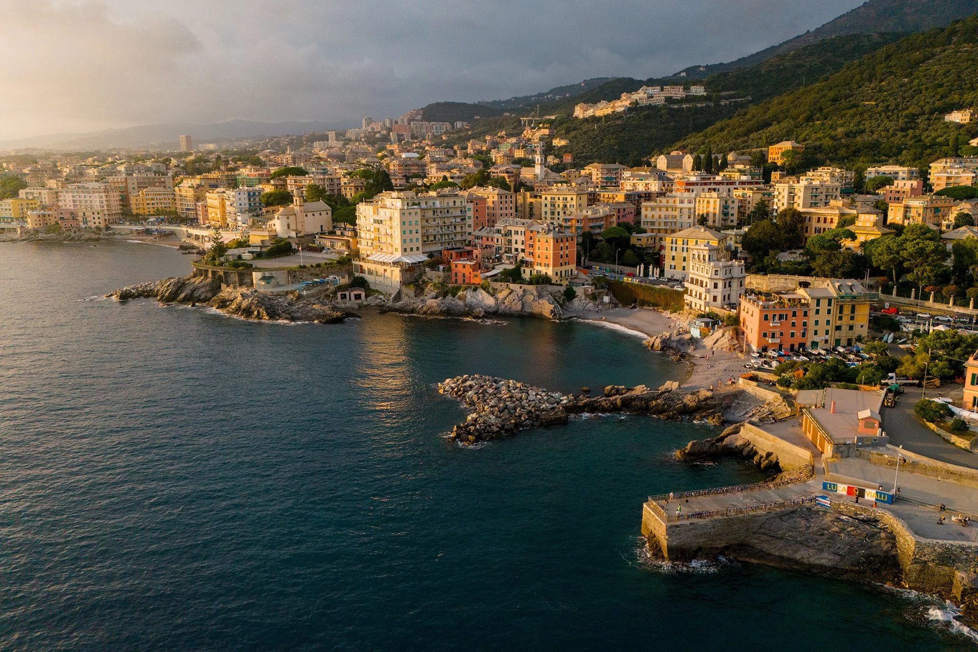 Paesaggio costiero di Vernazza, Italia, con edifici colorati lungo il mare e colline sullo sfondo.