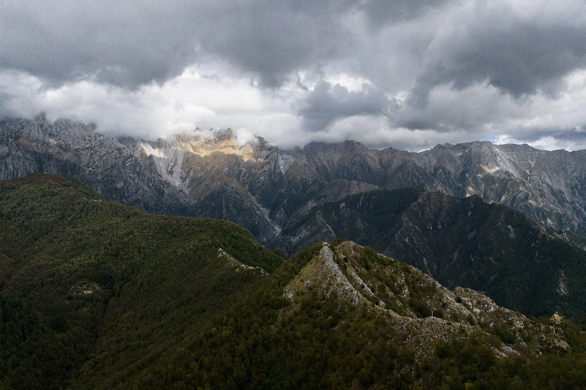 Montagne scoscese sotto un cielo nuvoloso, con alcune aree illuminate dalla luce del sole.