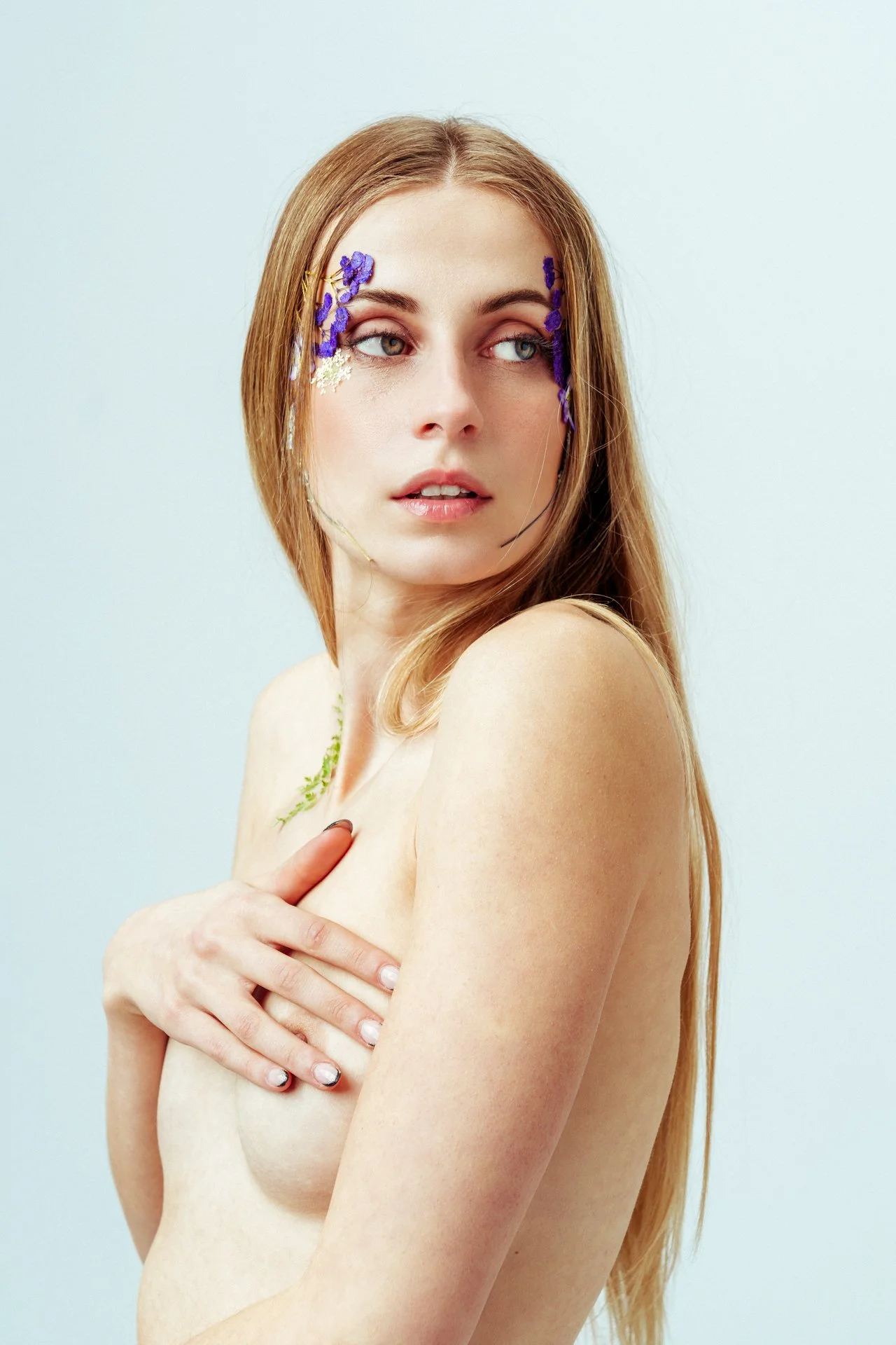 Ragazza con lunghi capelli rossi e decorazioni floreali sul volto, che si copre il petto con una mano.