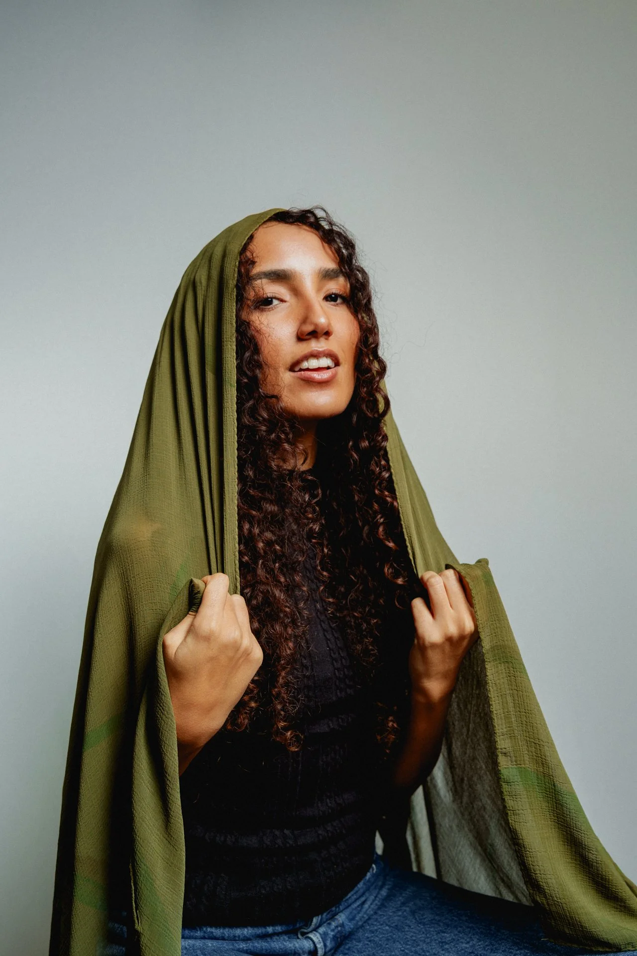 Ragazza con capelli riccioli che tiene il cappuccio verde di una giacca, sfondo neutro nudo.