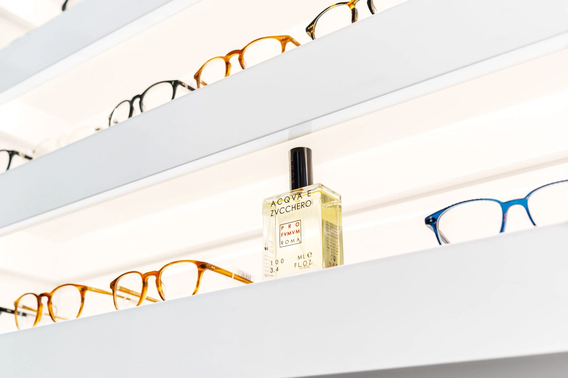 Lenti da vista di vari modelli e un flacone di profumo sulla mensola in una negozio di ottica.
