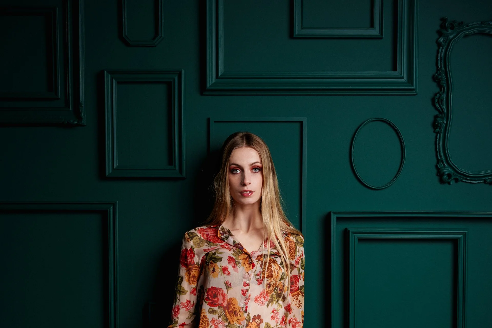 Ragazza con capello lungo e vestito floreale davanti a parete verde con pannelli decorativi.