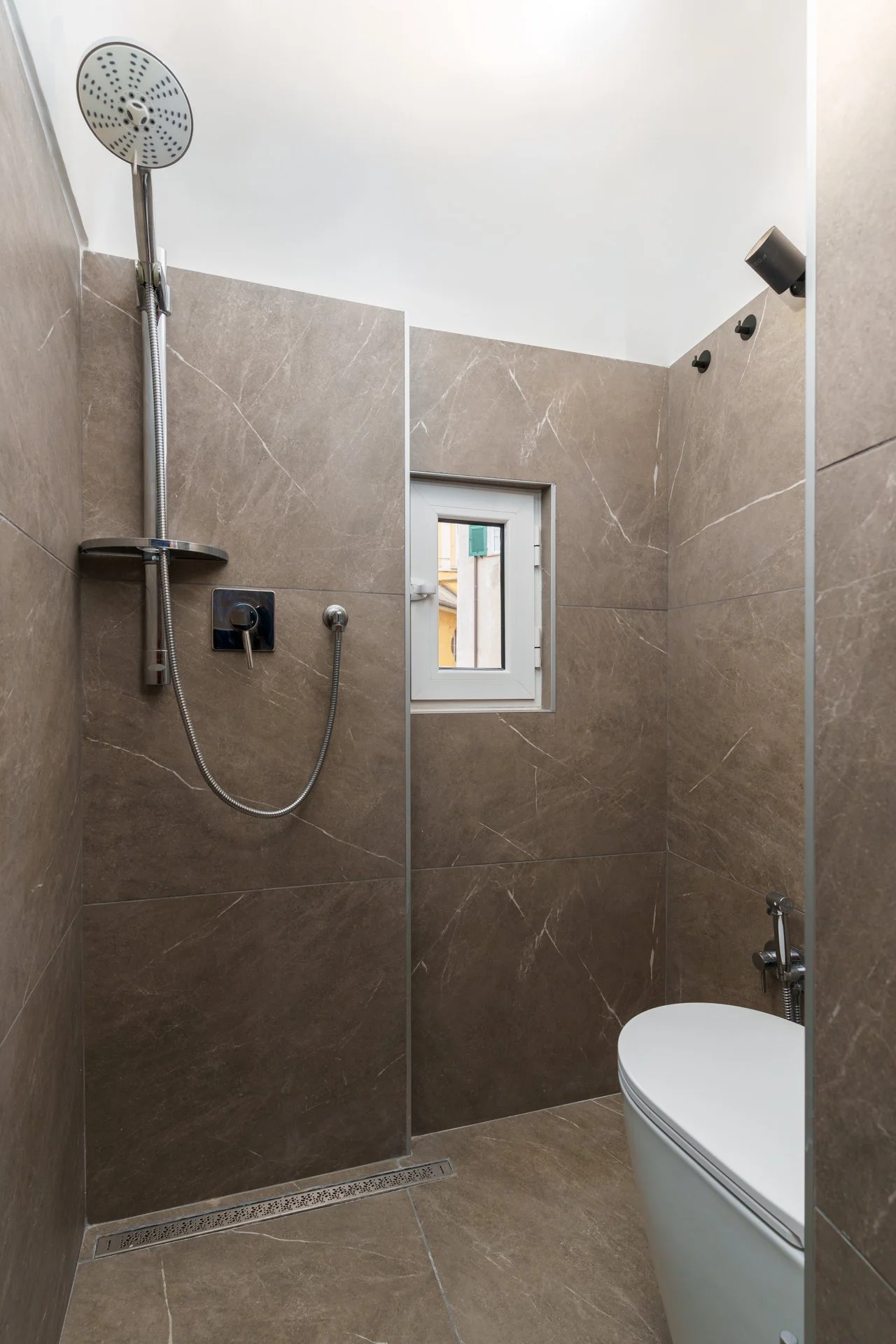 Doccia moderna con parete divisoria in vetro, con pioggia shower head, maniglia, e incluso un piccolo finestrino, tutte le superfici rivestite in piastrelle marroni.