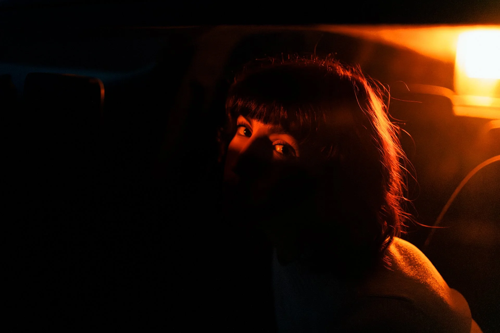 Ragazza con i capelli corti e lanciata da una luce calda, raggiante nel buio, che guarda verso l'obiettivo.