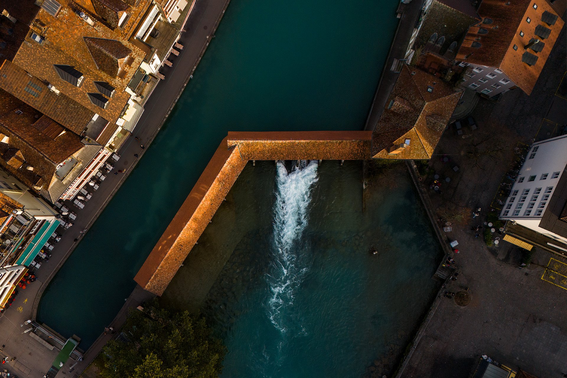 Vista aerea di un canale cittadino con una cascata artificiale al centro, circondato da edifici residenziali e commerciali.