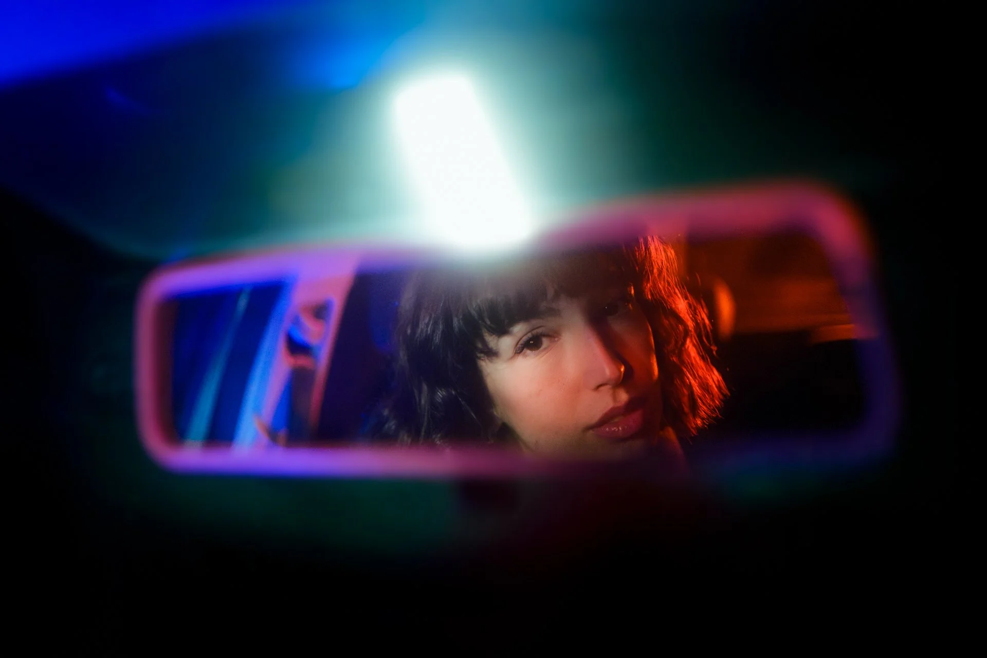 Ragazza con capelli ricciolini guarda nello specchietto retrovisore con luci colorate