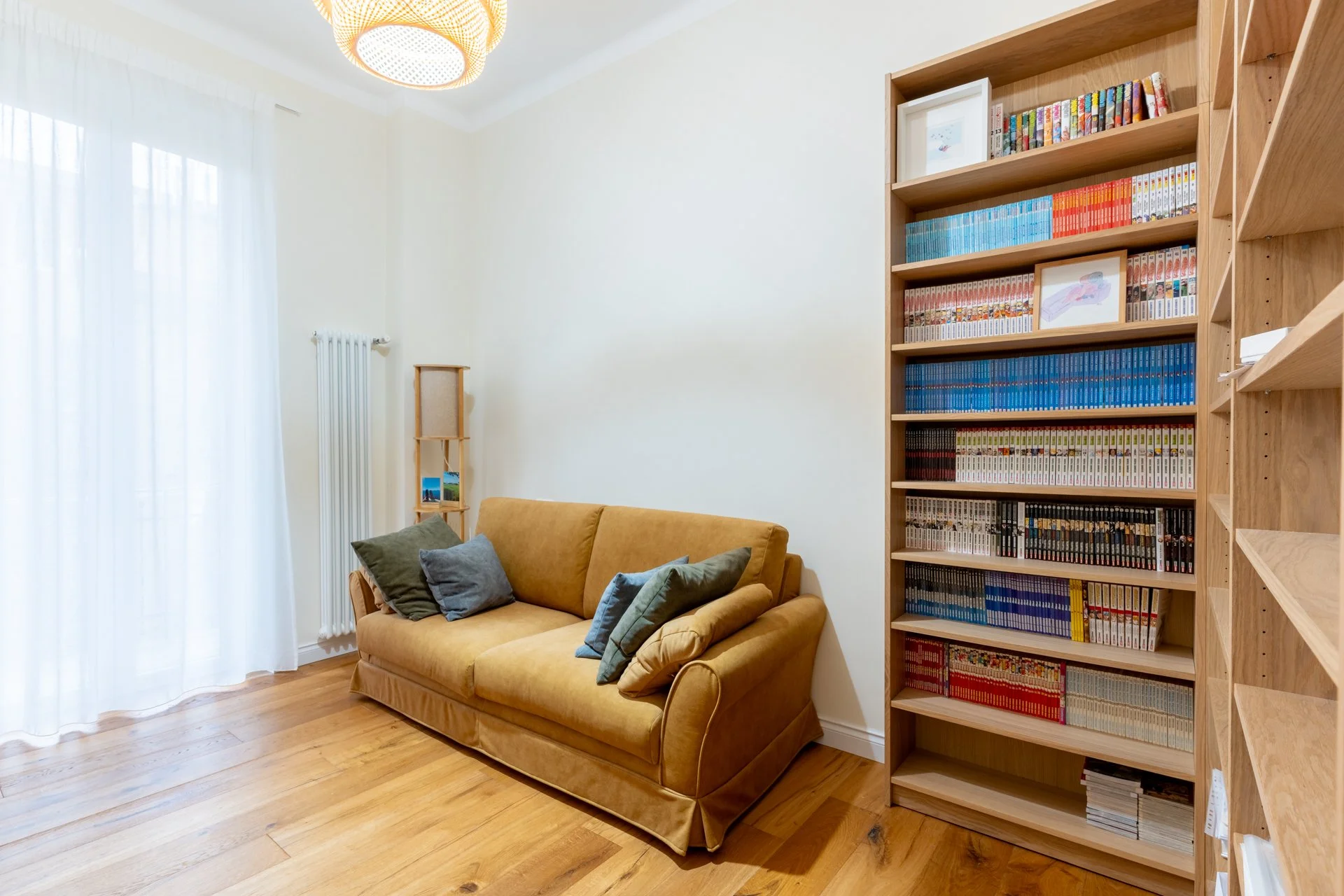 Soggiorno con divano beige, cuscini verdi e grigi, libreria di legno con libri e quadri.