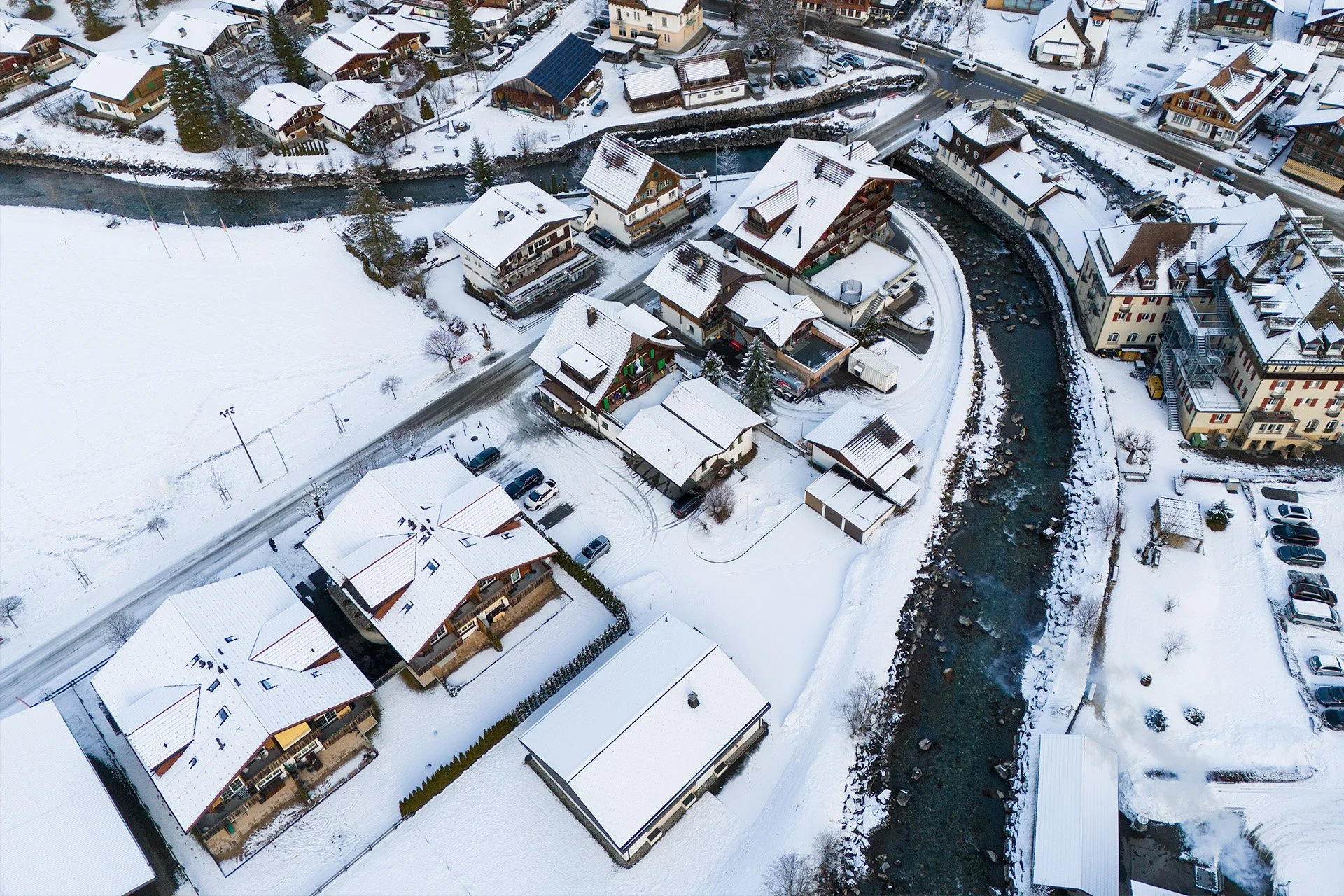 Veduta aerea di case di montagna innevate e un fiume che attraversa il paesaggio in inverno.
