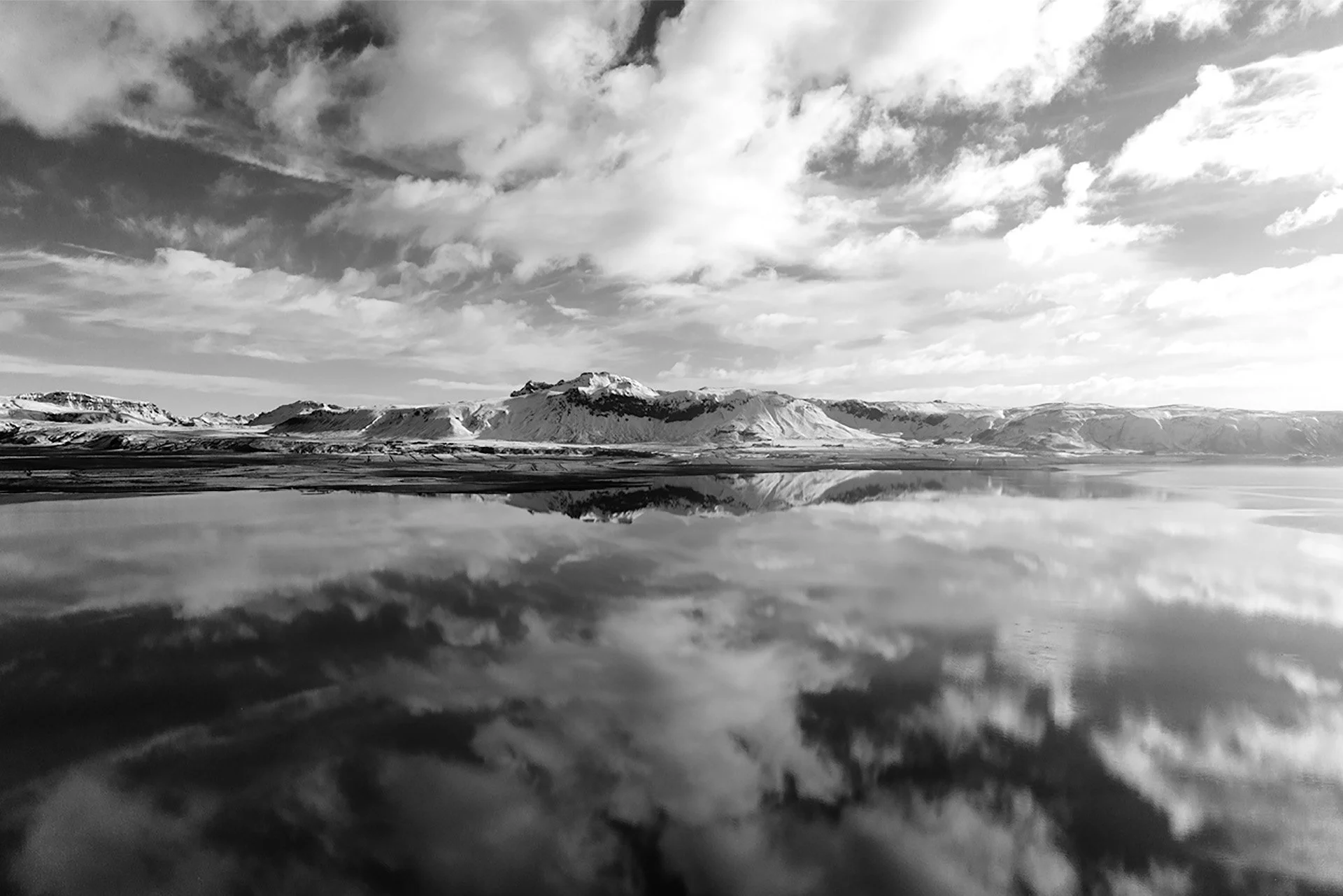 Paesaggio montano con neve, riflesso delle montagne in un lago, cielo con nuvole.