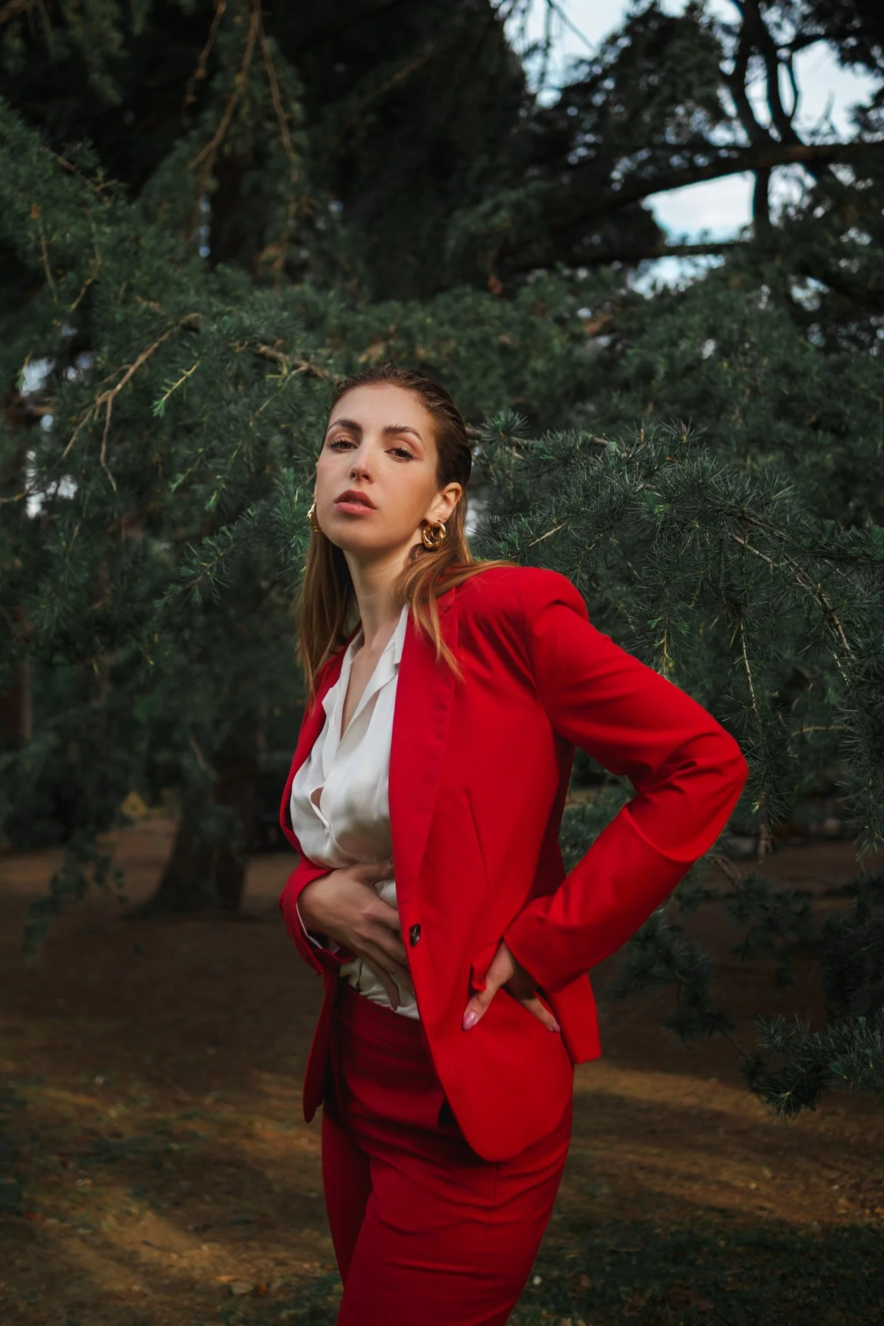 Una donna in abbigliamento elegante di colore rosso posa in un ambiente naturale con alberi verdi sullo sfondo