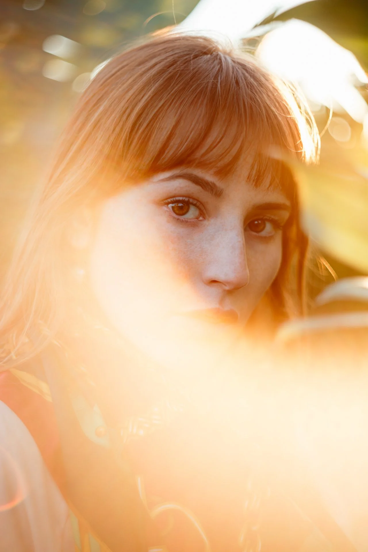 Ragazza con capelli castani rossi, occhi marroni, in un ambiente esterno con luce solare calda, tra foglie e natura.