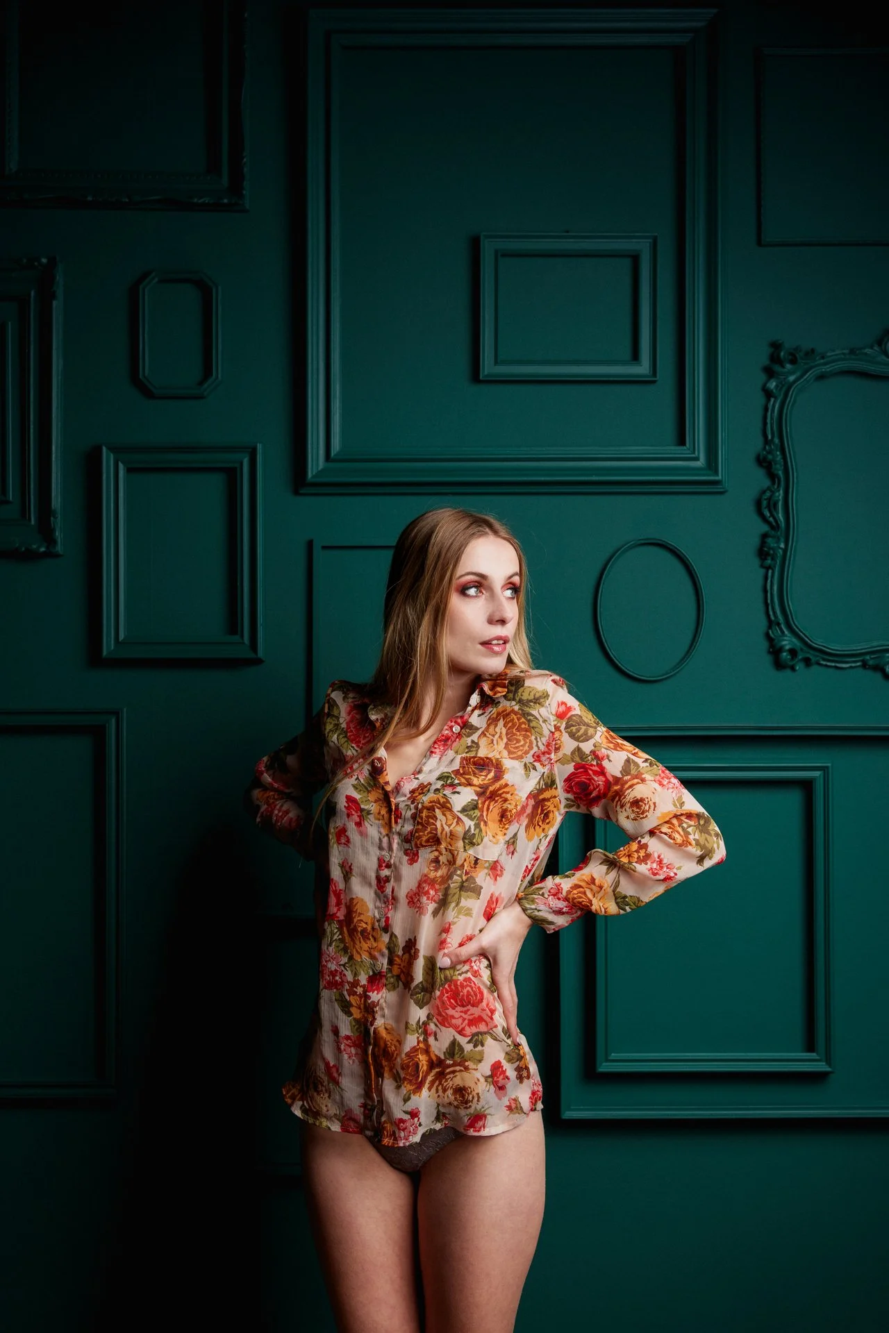 Donna con camicia floreale che posa davanti a una parete verde con decorazioni.