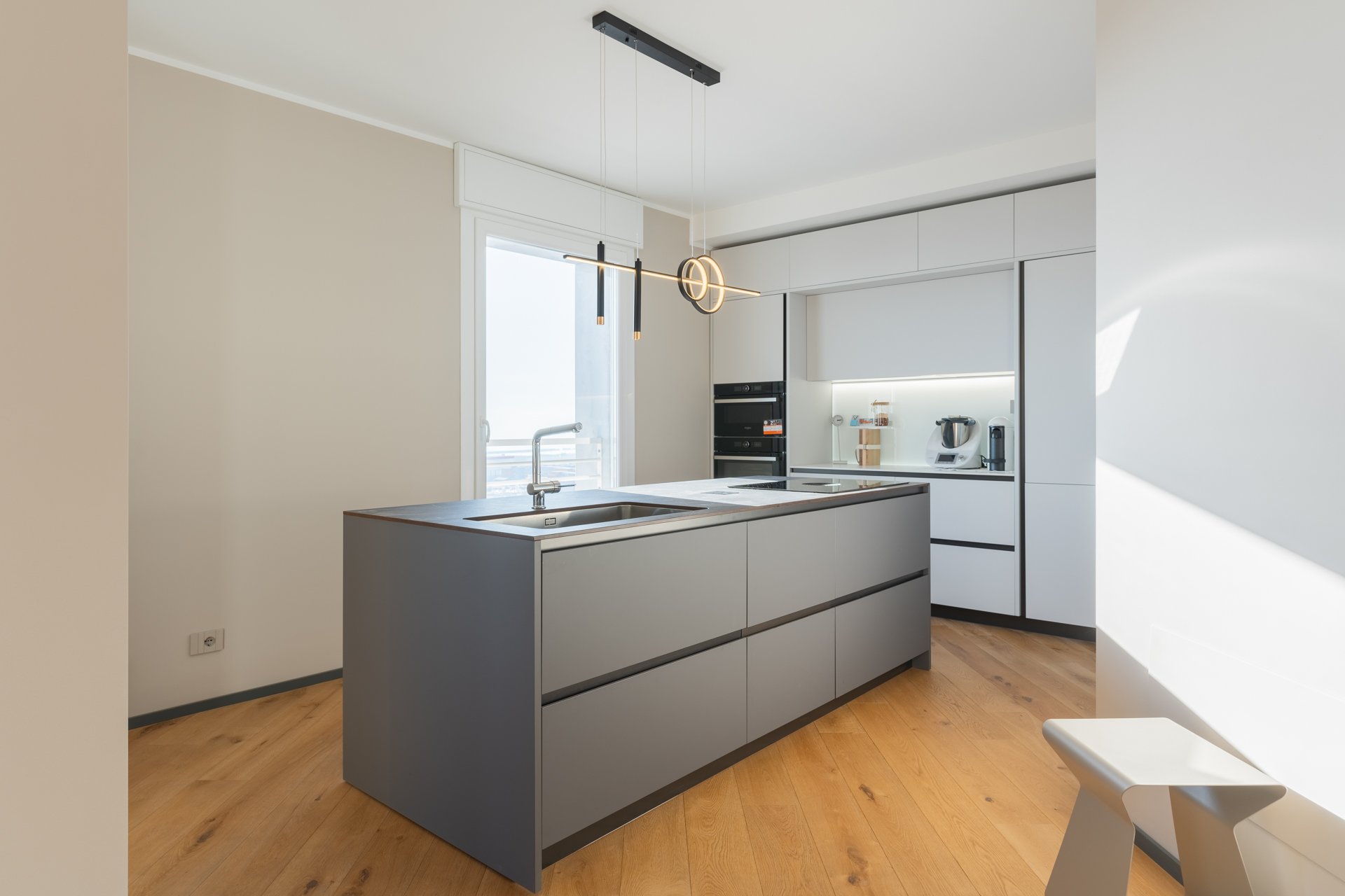 Cucina moderna con isola grigia, armadi bianchi, forno e microonde integrati, e una macchina da caffè pointed