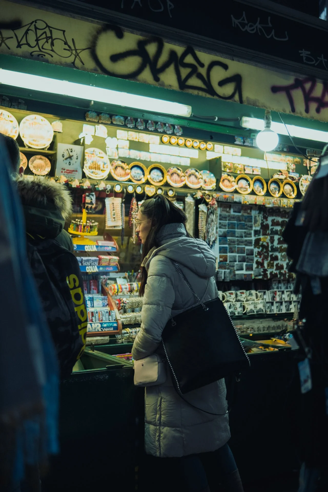 Persone che fanno acquisti in un chiosco di street food con decorazioni di piatti colorati e illuminazione intensa.