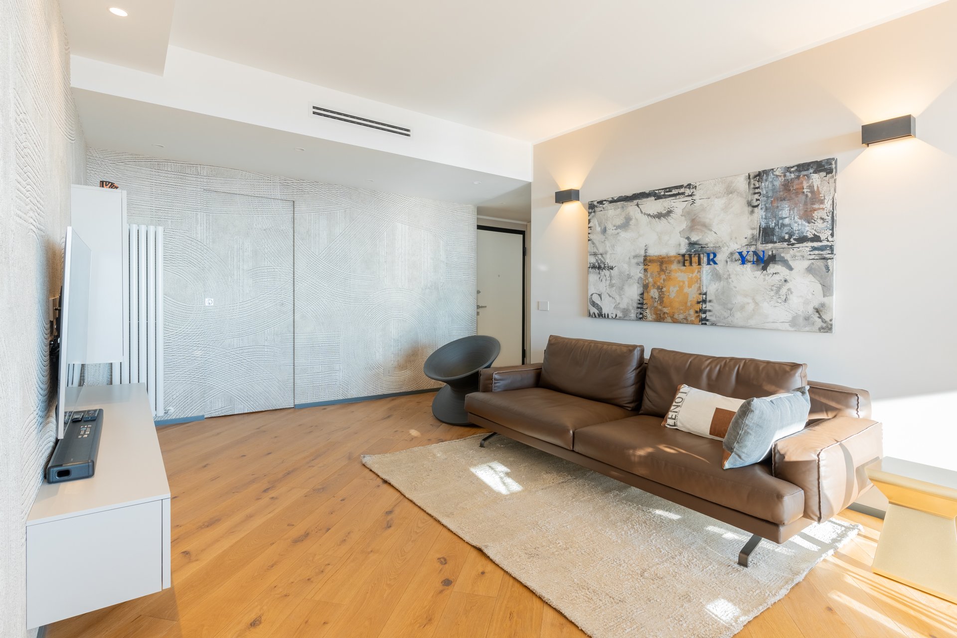 Interno di un soggiorno moderno con divano marrone, parete decorativa, quadri astratti, tappeto beige e lampade da parete