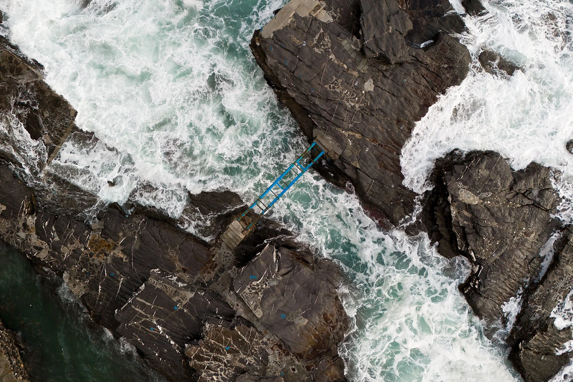 Immagine aerea di scogli e onde che si infrangono.