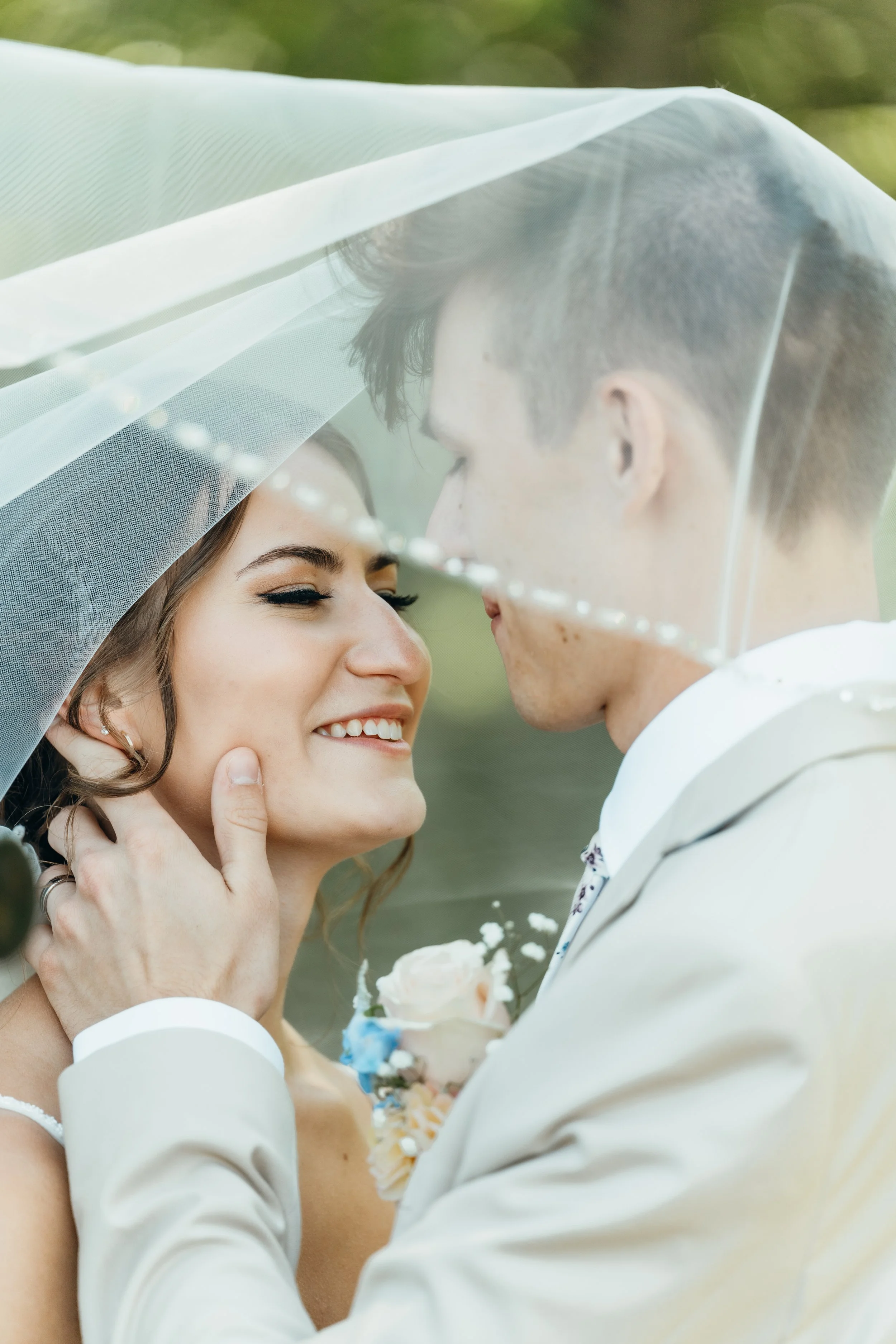 Bride and groom under veil, smiling intimately at each other