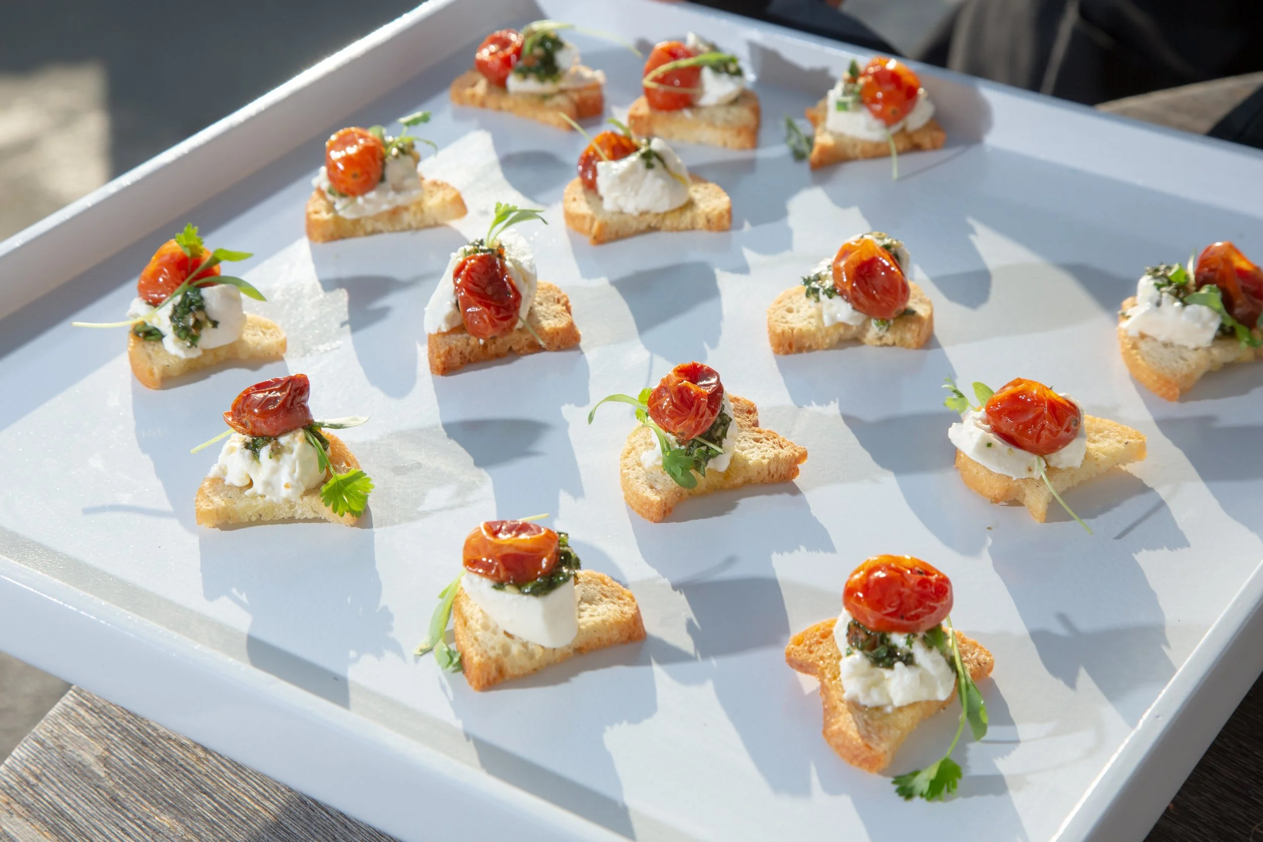 Tray of crostini appetizers with goat cheese, roasted cherry tomatoes, and herbs on toasted bread.