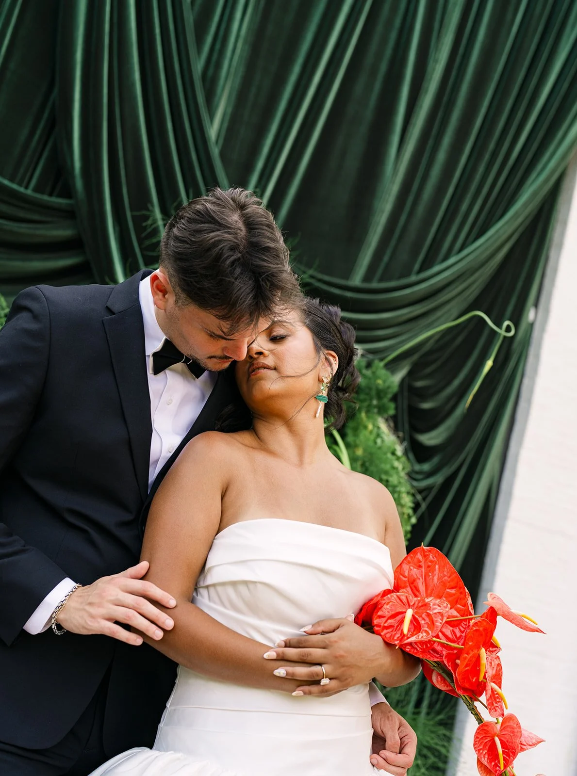A wedding couple in front of a green draped background