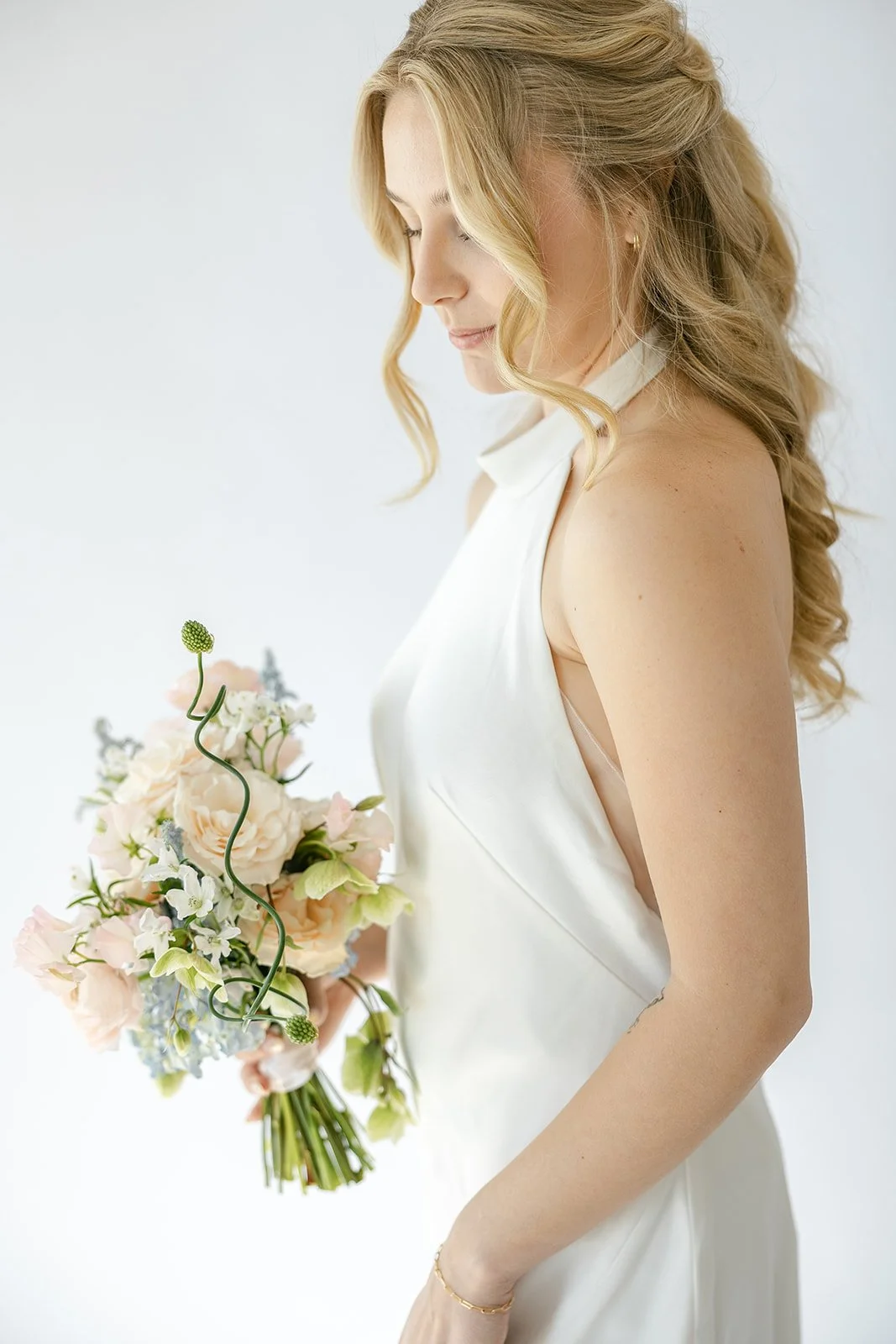 A girl in a satin, halter neck wedding dress with a bouquet