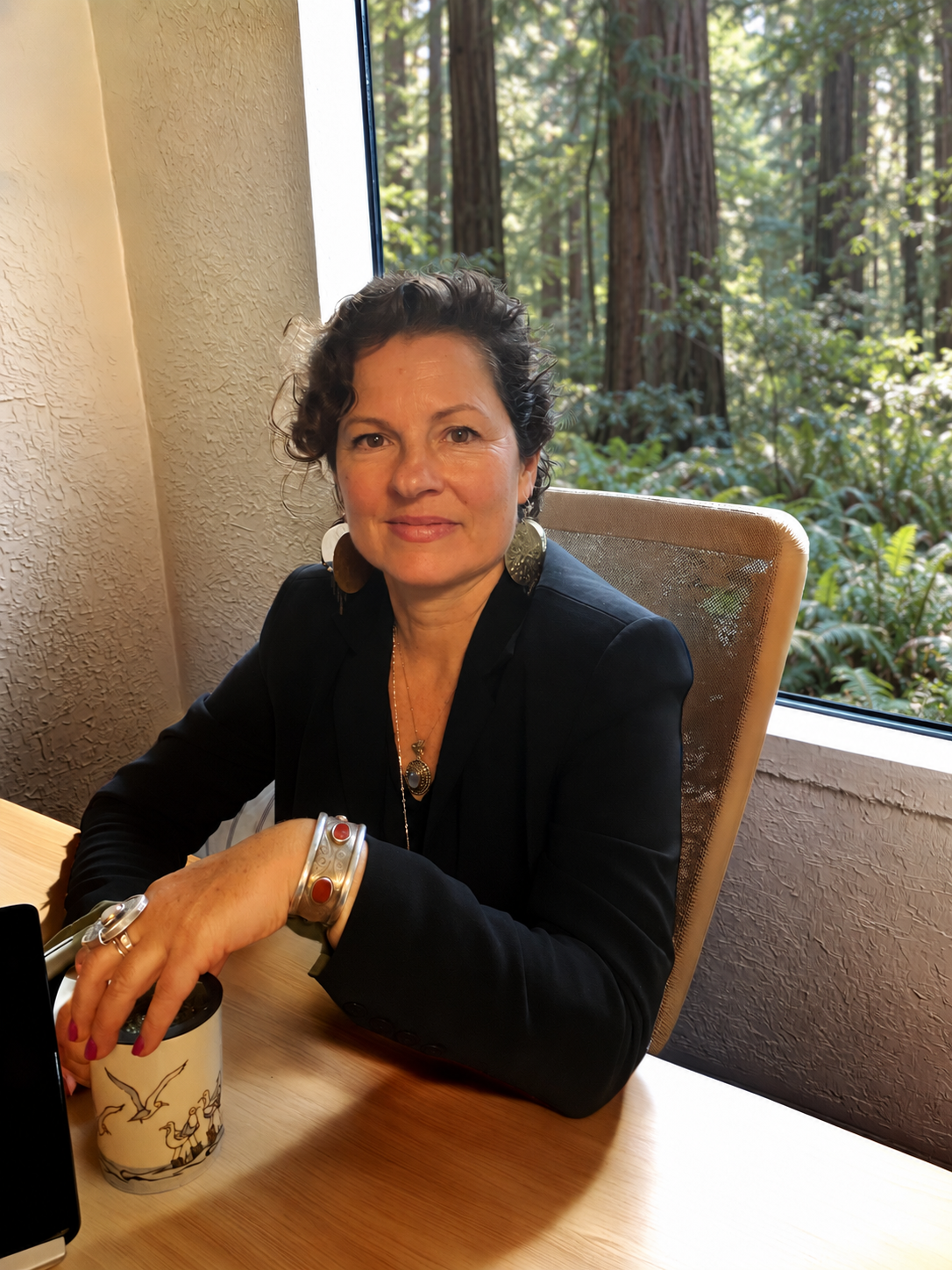 Lavender Grace Kent seated at her desk with Mendocino Coast redwoods visible through the window.