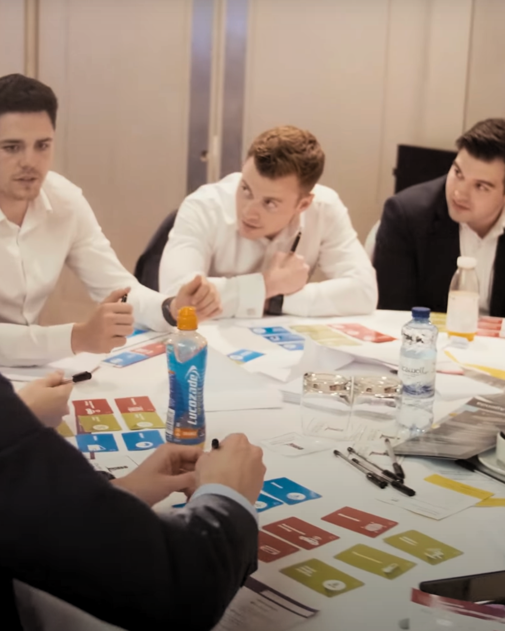 Businessmen sitting around a table during a meeting, discussing with game cards and markers on the table.