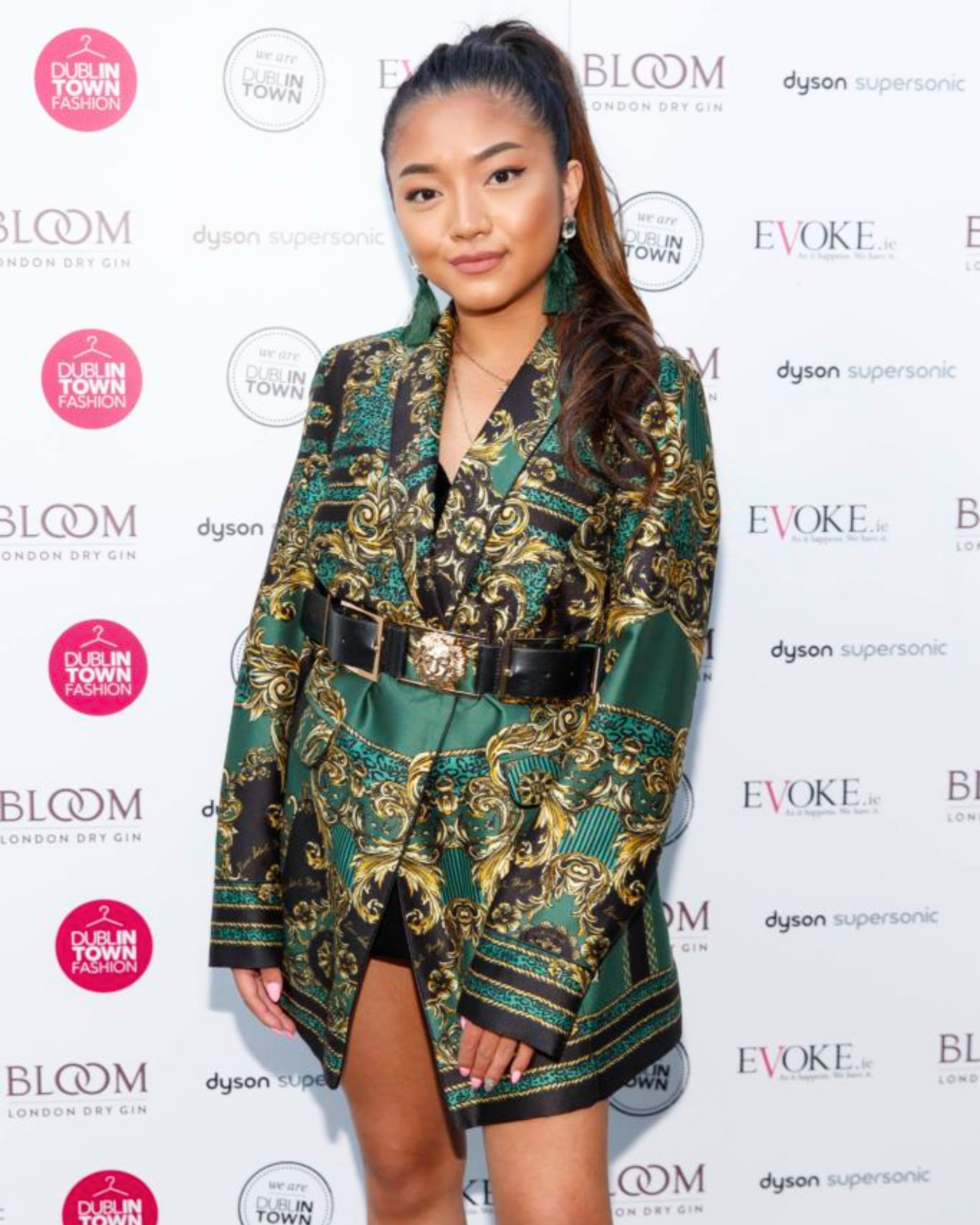 Young woman in patterned blazer with belt posing at fashion event.