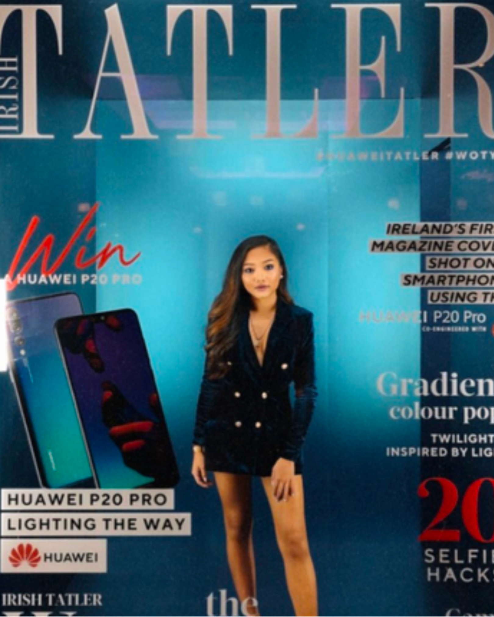 A woman in a black dress standing in front of a blue magazine cover. The cover features a phone and text about Huawei P20 Pro and a contest. The magazine name is partially visible at the top.