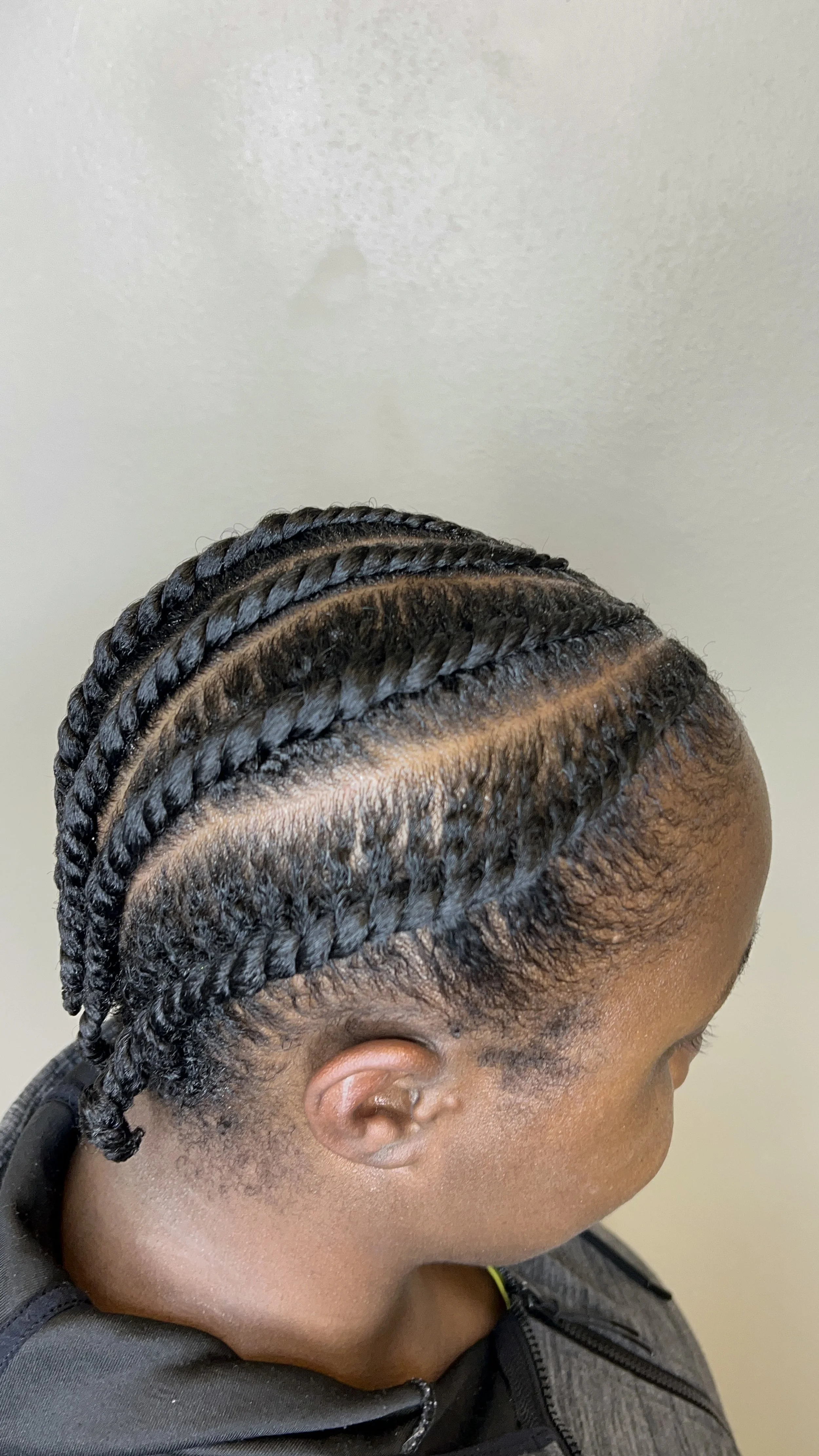 A woman with neatly braided hairstyle, showing multiple rows of braids running from the front to the back of her head.