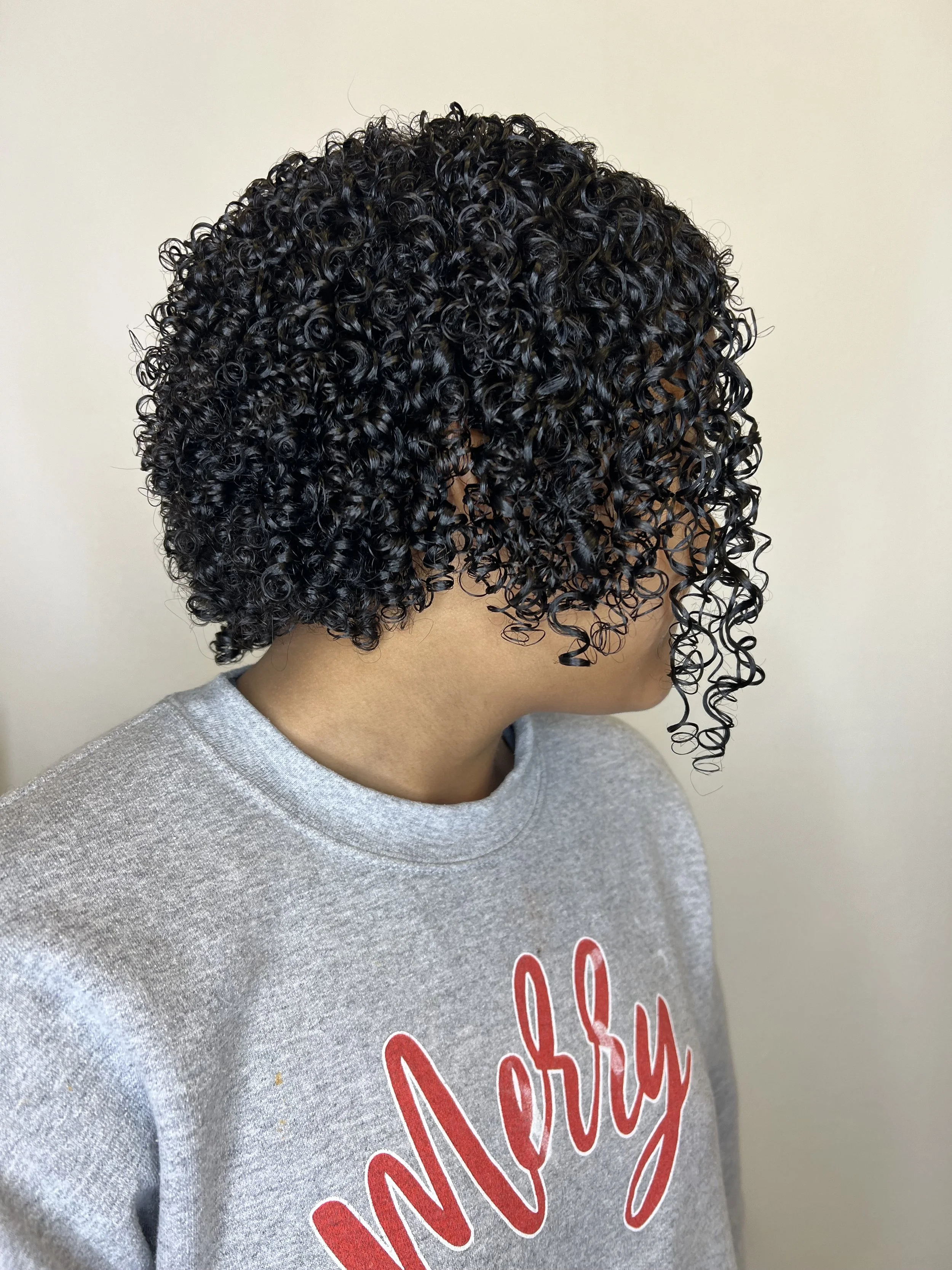 Side view of a woman with short, curly black hair, wearing a gray sweatshirt with red text that says 'Mercy'.