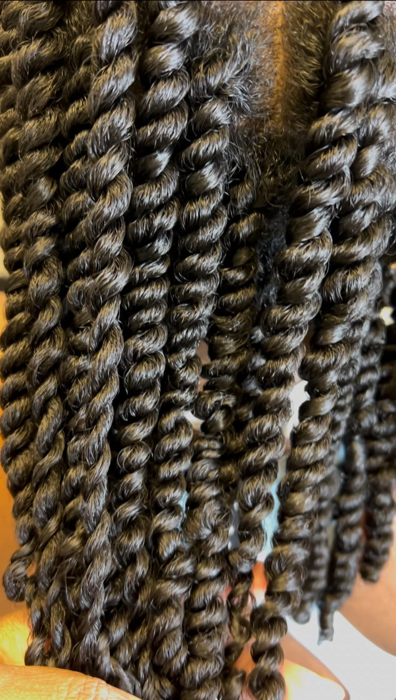 Close-up of dark brown twisted faux locs hairstyle with a New York Knicks cap visible in the background.