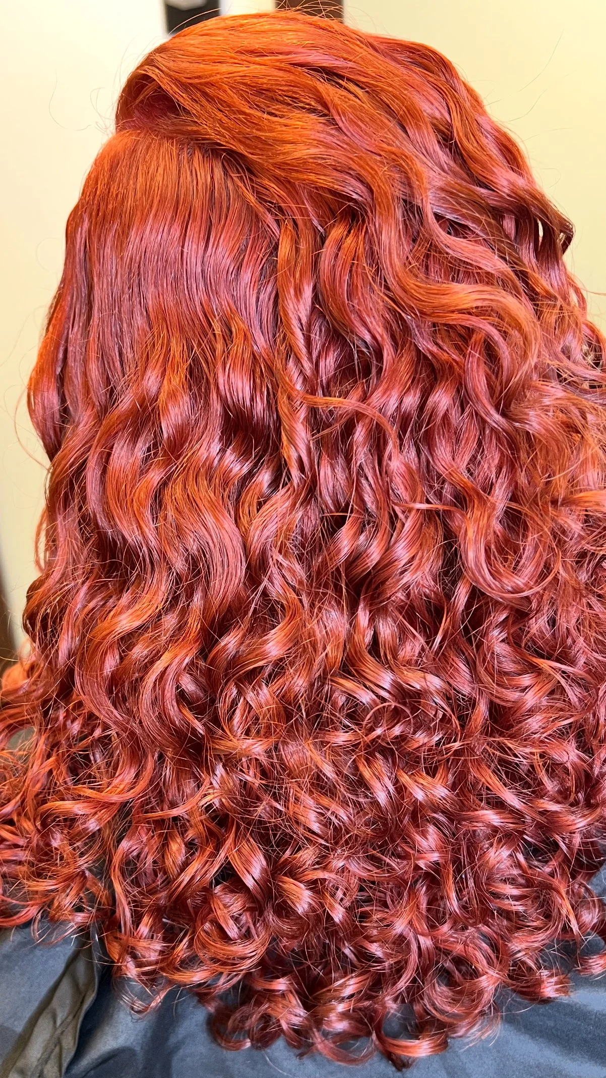 Back view of a person with vibrant red, curly, and wavy hair.