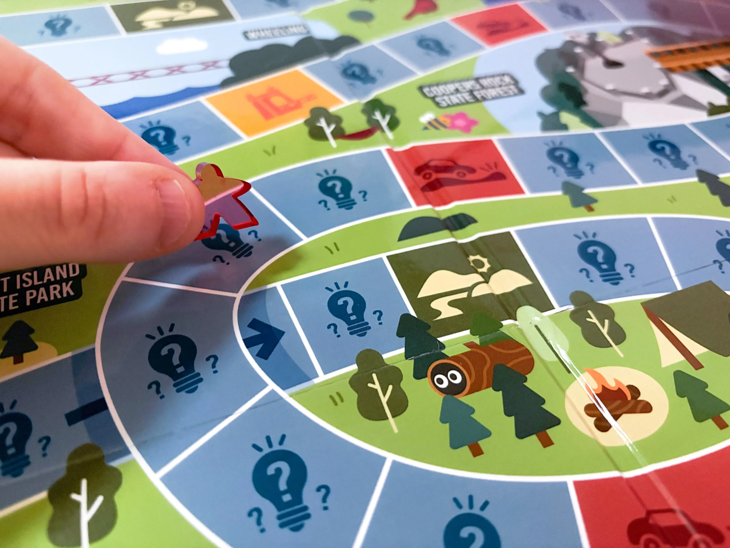 Close-up of a player moving a game piece along the illustrated Mountain Moves board through West Virginia destinations.