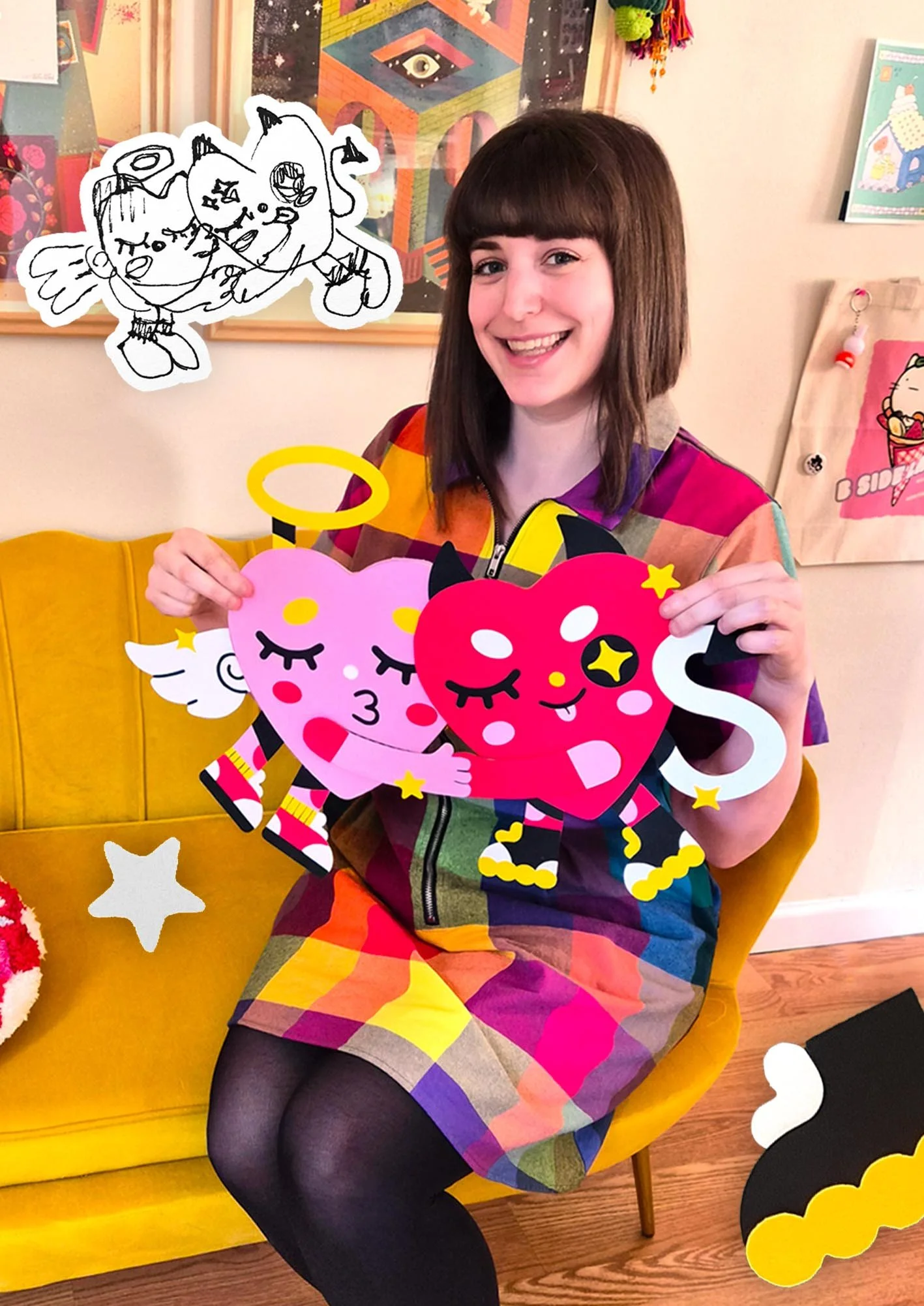 A woman with a bob haircut is sitting on a yellow chair, smiling, and holding paper cutouts of cartoon-style unicorns with hearts and star accents. There are festive decorations and colorful artwork in the background.