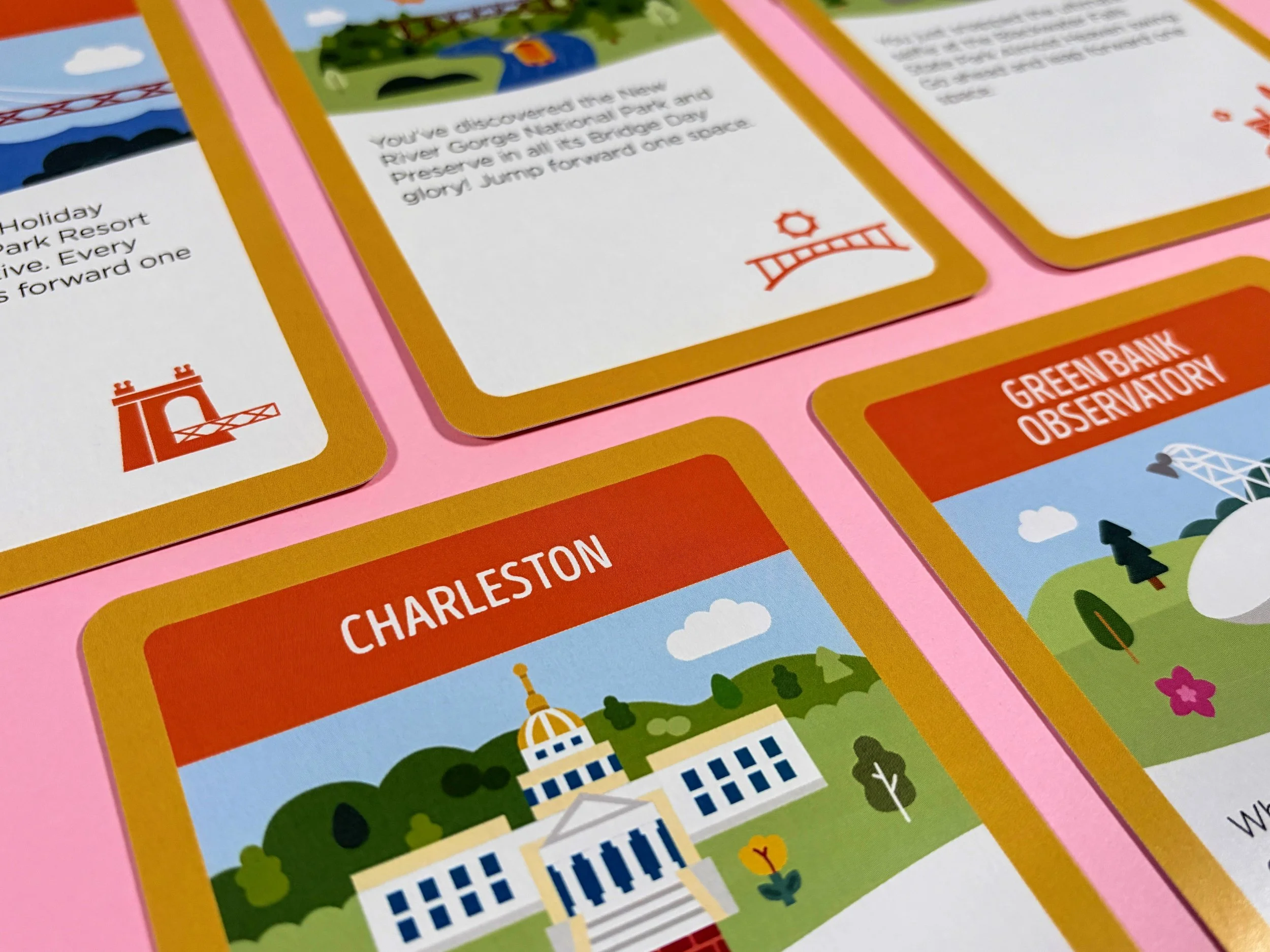 Close-up of colorful cards from a board game, featuring the Golden Gate Bridge, buildings, and scenery of Charleston, with some text and icons visible.