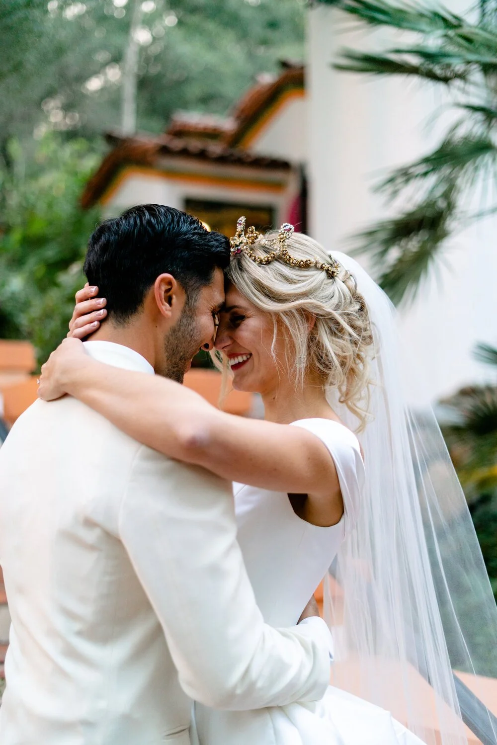 A bride and groom embrace, the bride's hair worn up with a jewelled headpiece and veil