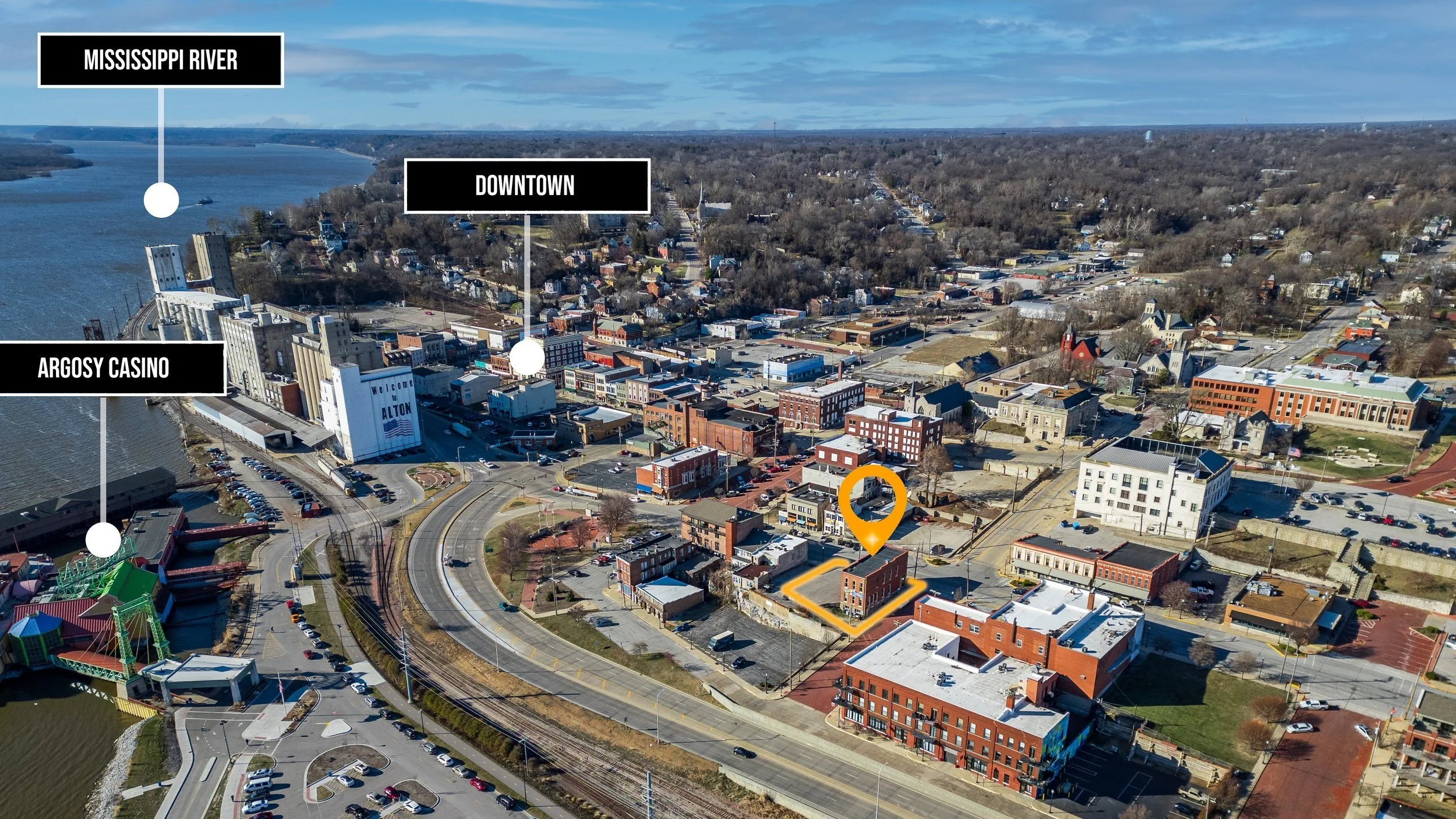 Aerial view of Alton, Illinois, showing the Mississippi River to the west, Argosy Casino near the riverbank, the downtown area with various buildings and streets, and a marker indicating a specific building on the right side of the image.