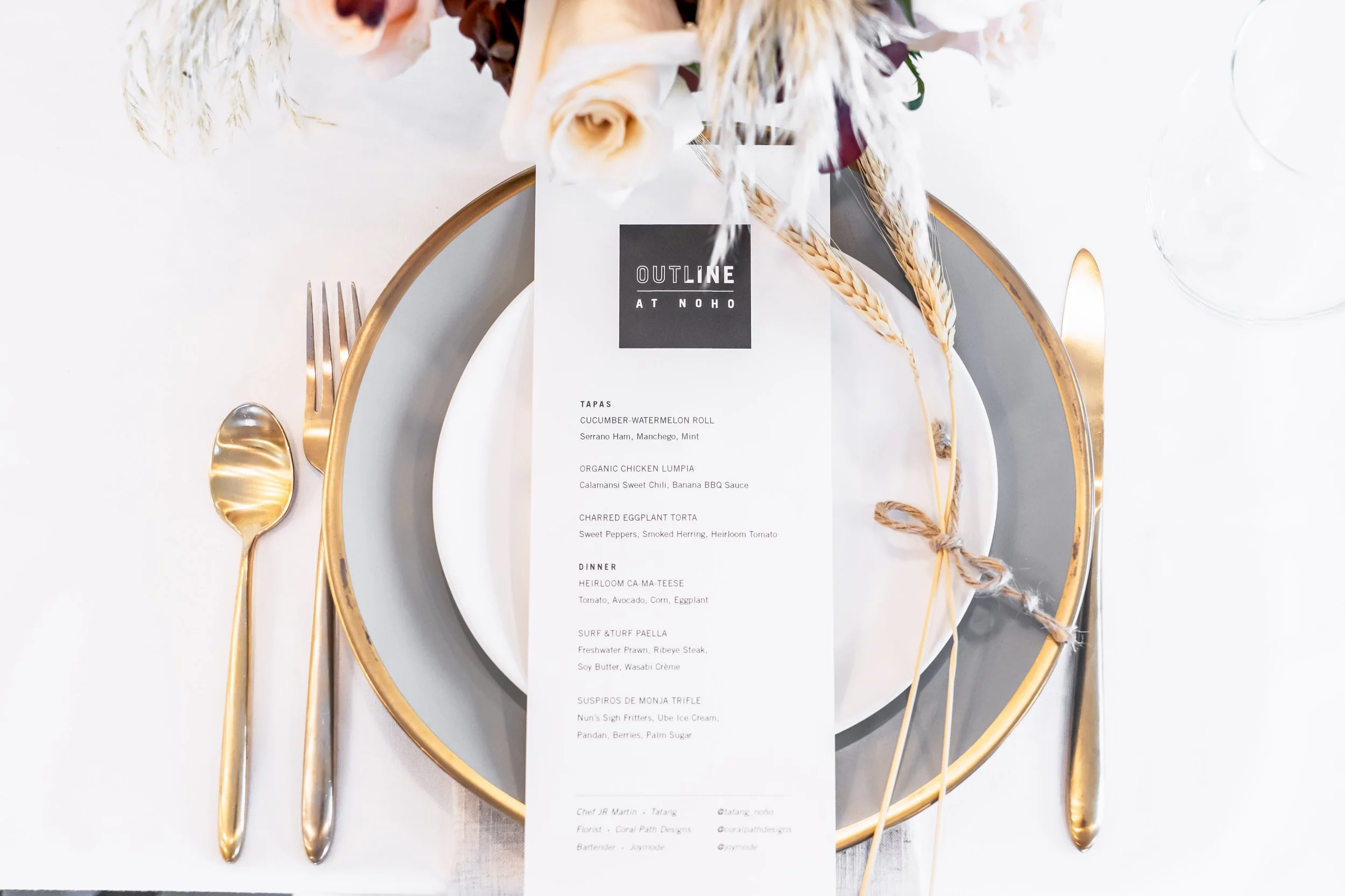 Press Event. Elegant table setting with a gold-rimmed plate, gold cutlery, and a floral centerpiece; place card with a printed menu from Outline at NOHO.