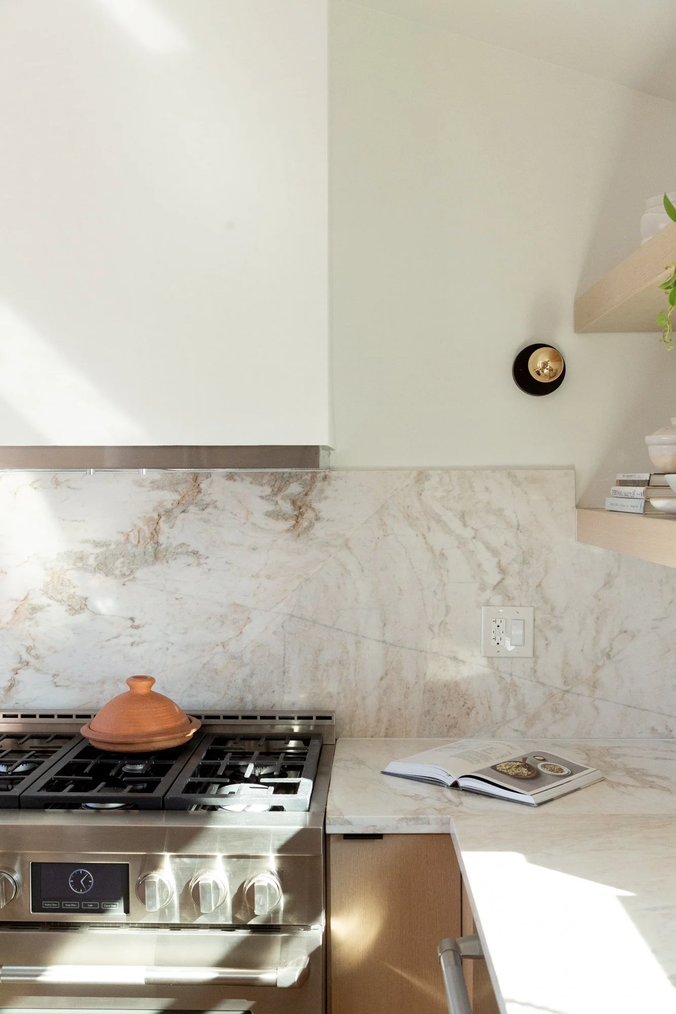 High-quality photography and videography for real estate. Kitchen with marble backsplash, stainless steel stove, an open cookbook on counter, and a terracotta pot on stove.