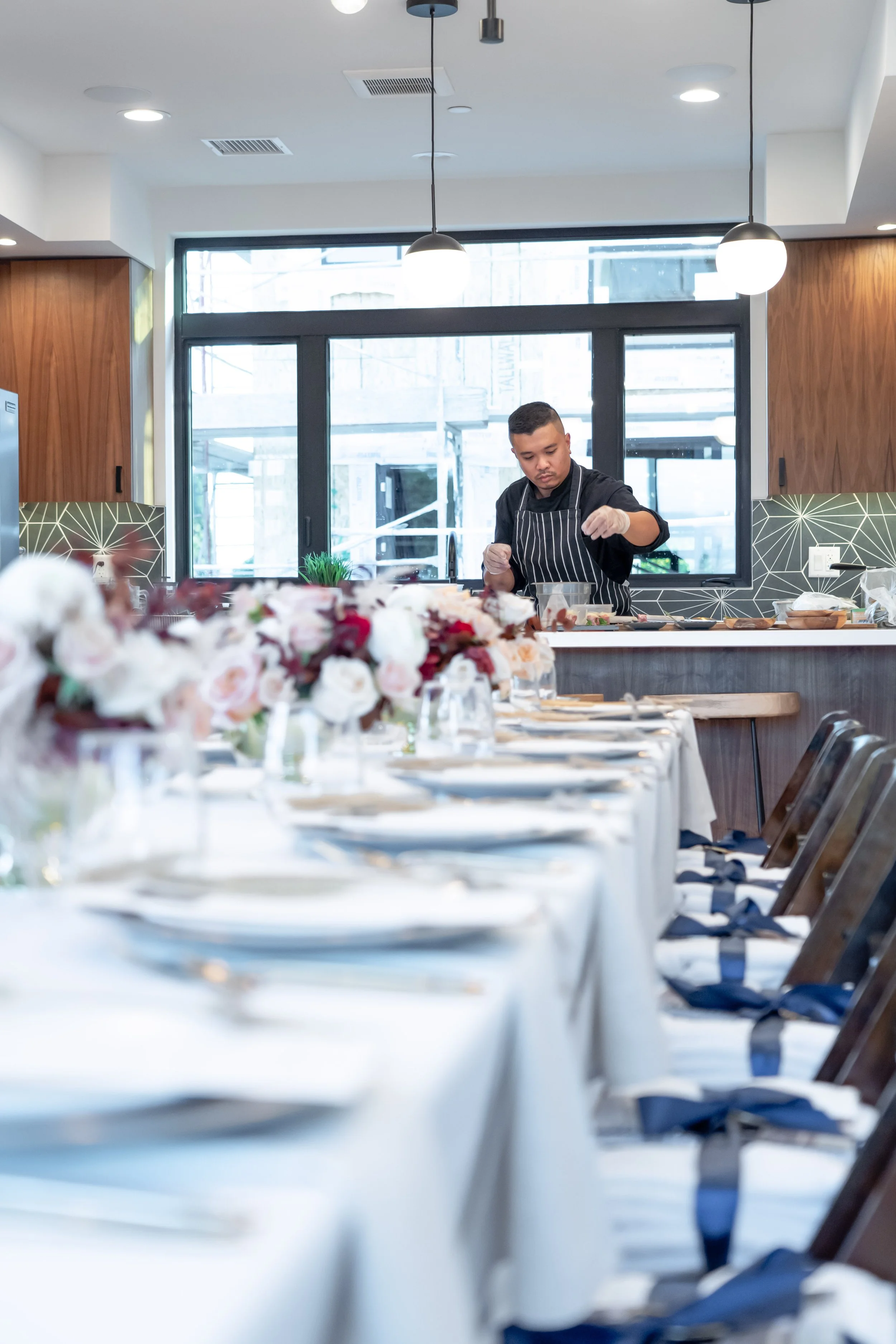 Press Release Party with a commissioned chef preparing food behind a dining table set with white plates, glasses, and floral centerpieces in Outline At Noho, a new real estate development in North Hollywood